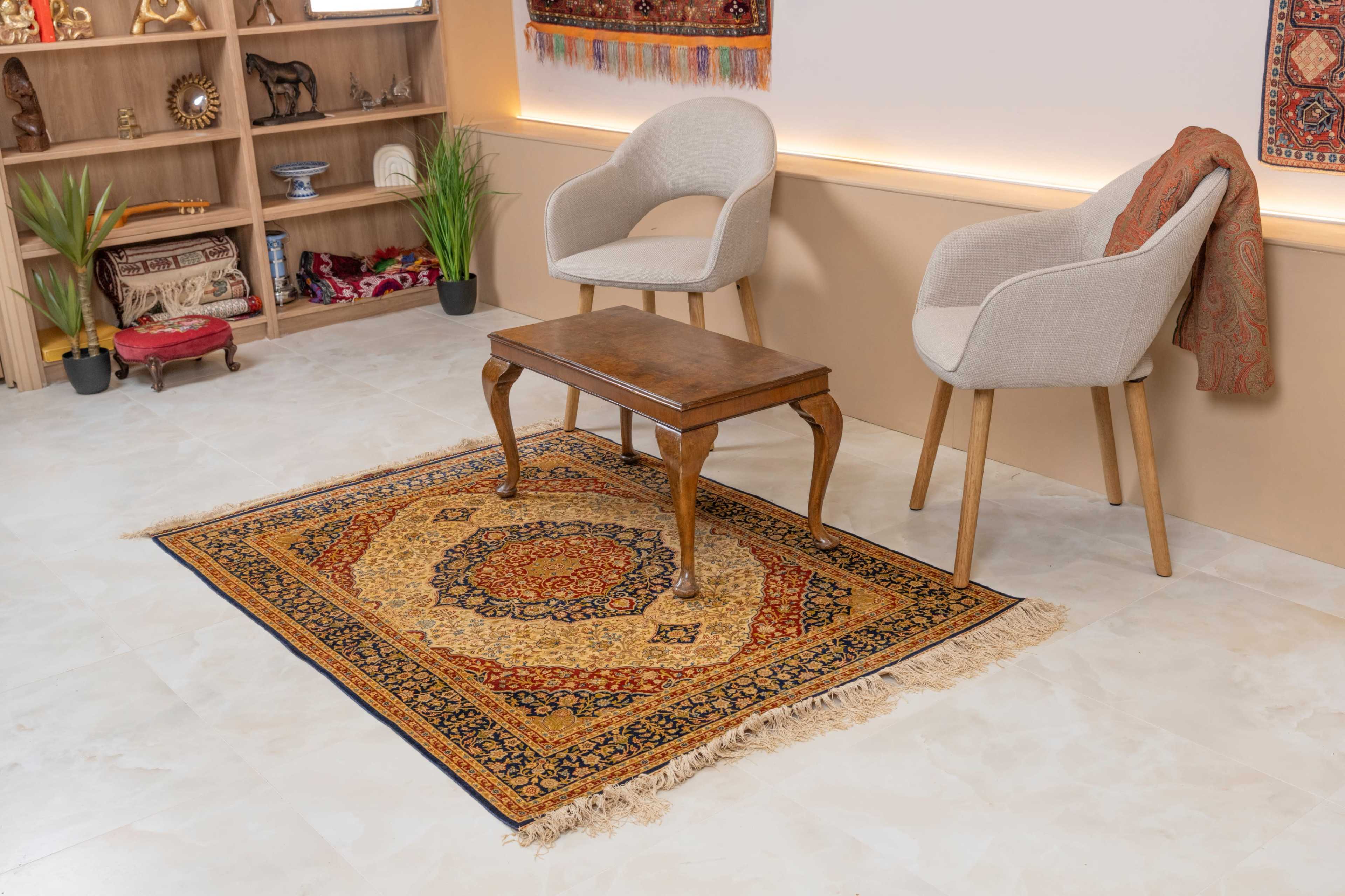 The image shows a cozy interior space featuring two light-colored chairs, a small wooden table, and a decorative rug on a tiled floor.