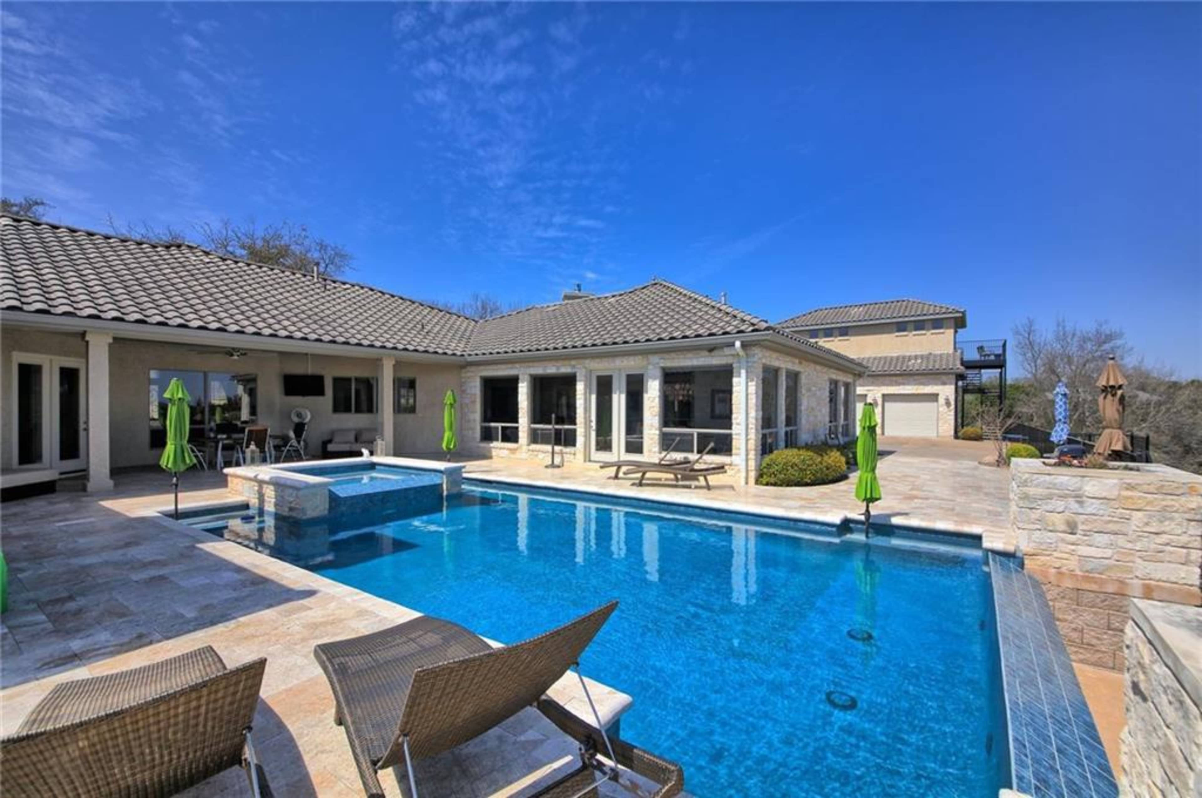 A residential backyard featuring a swimming pool, patio furniture, and a modern house with a tiled roof.