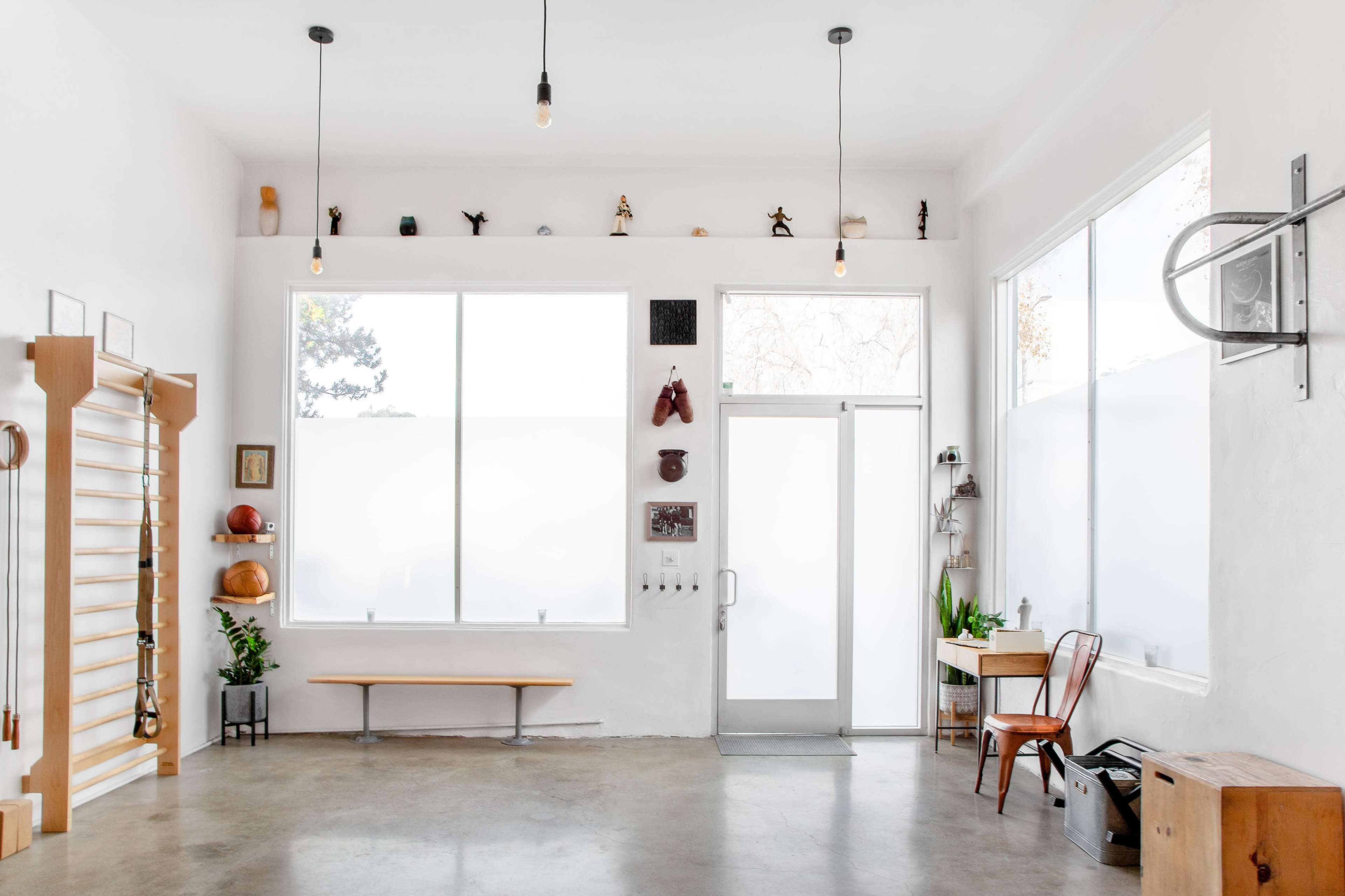 A bright, minimalistic interior studio with a wooden bench, large windows, and various decorative items on the walls.
