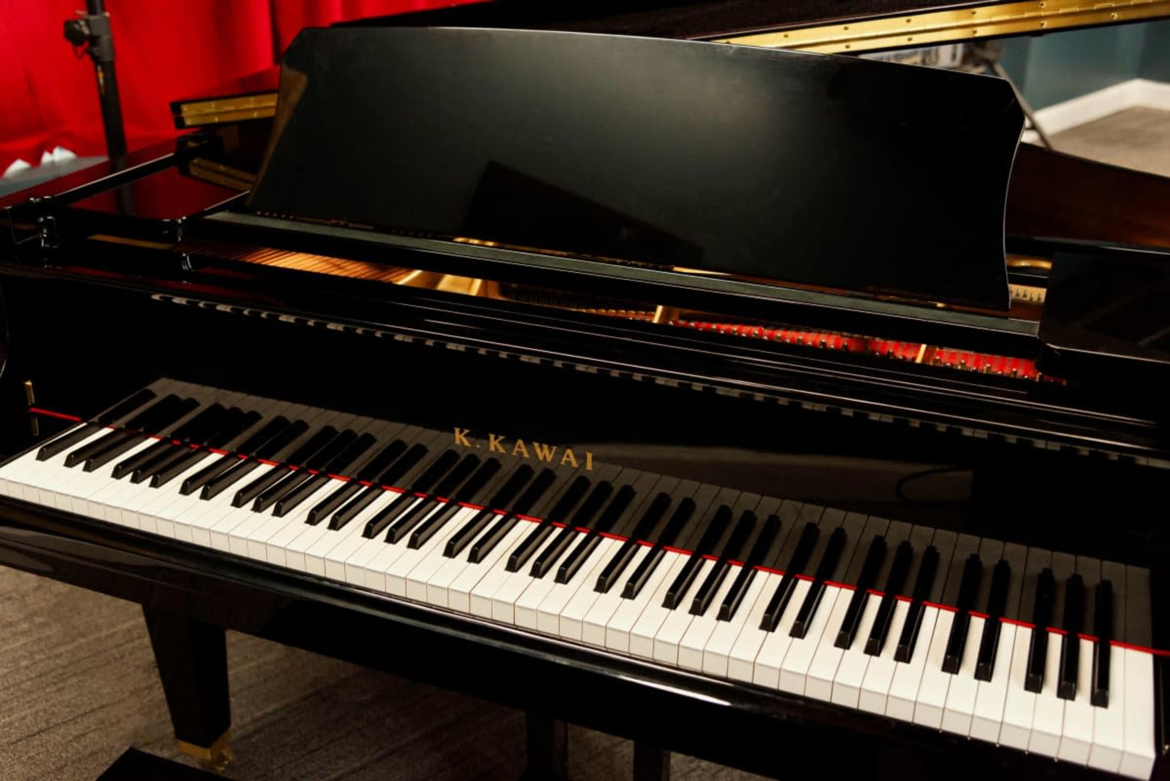 A Kawai grand piano with a polished black finish sits in a room with red curtains.