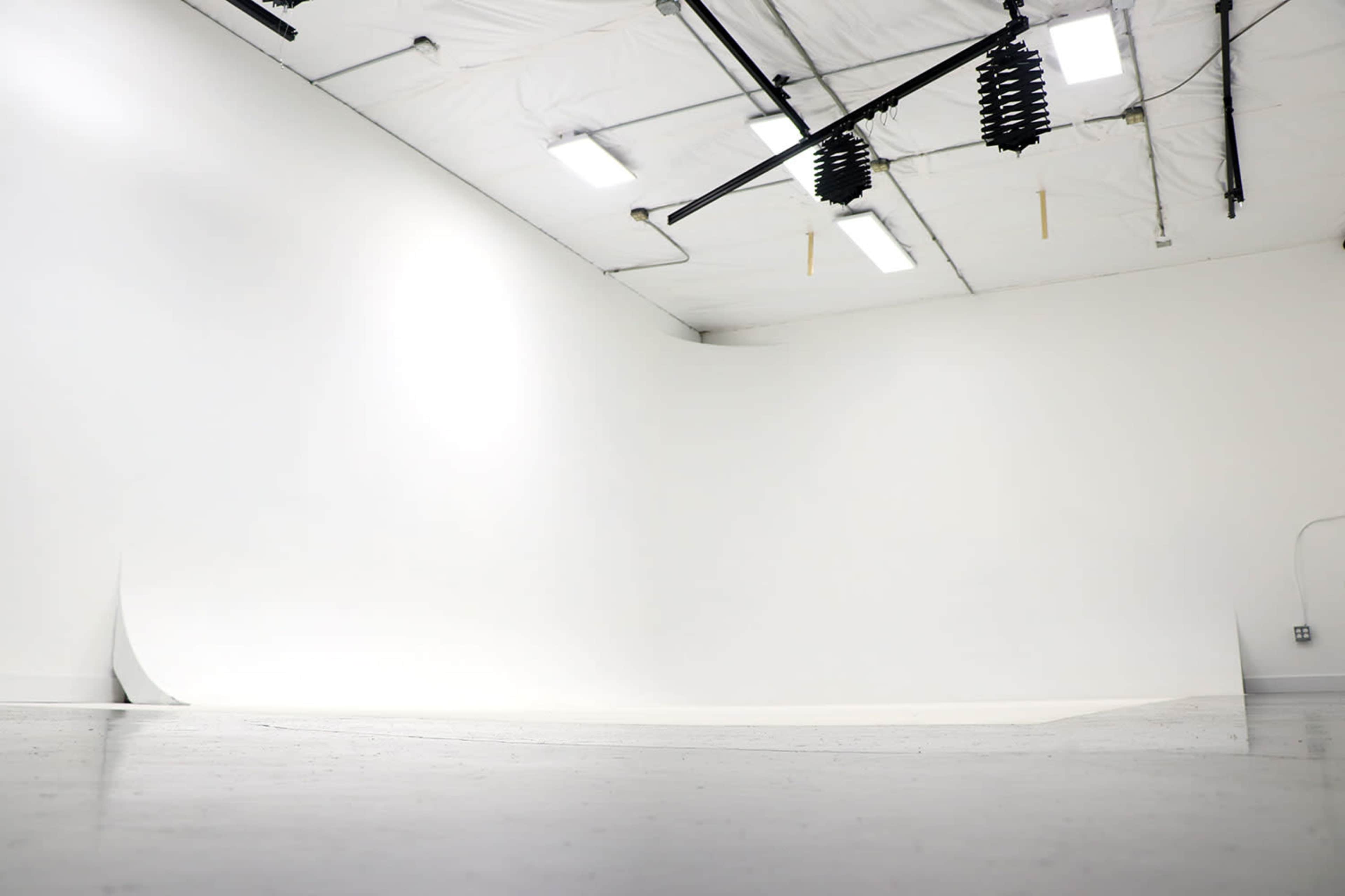 A spacious, empty studio with a seamless white backdrop and overhead lighting.