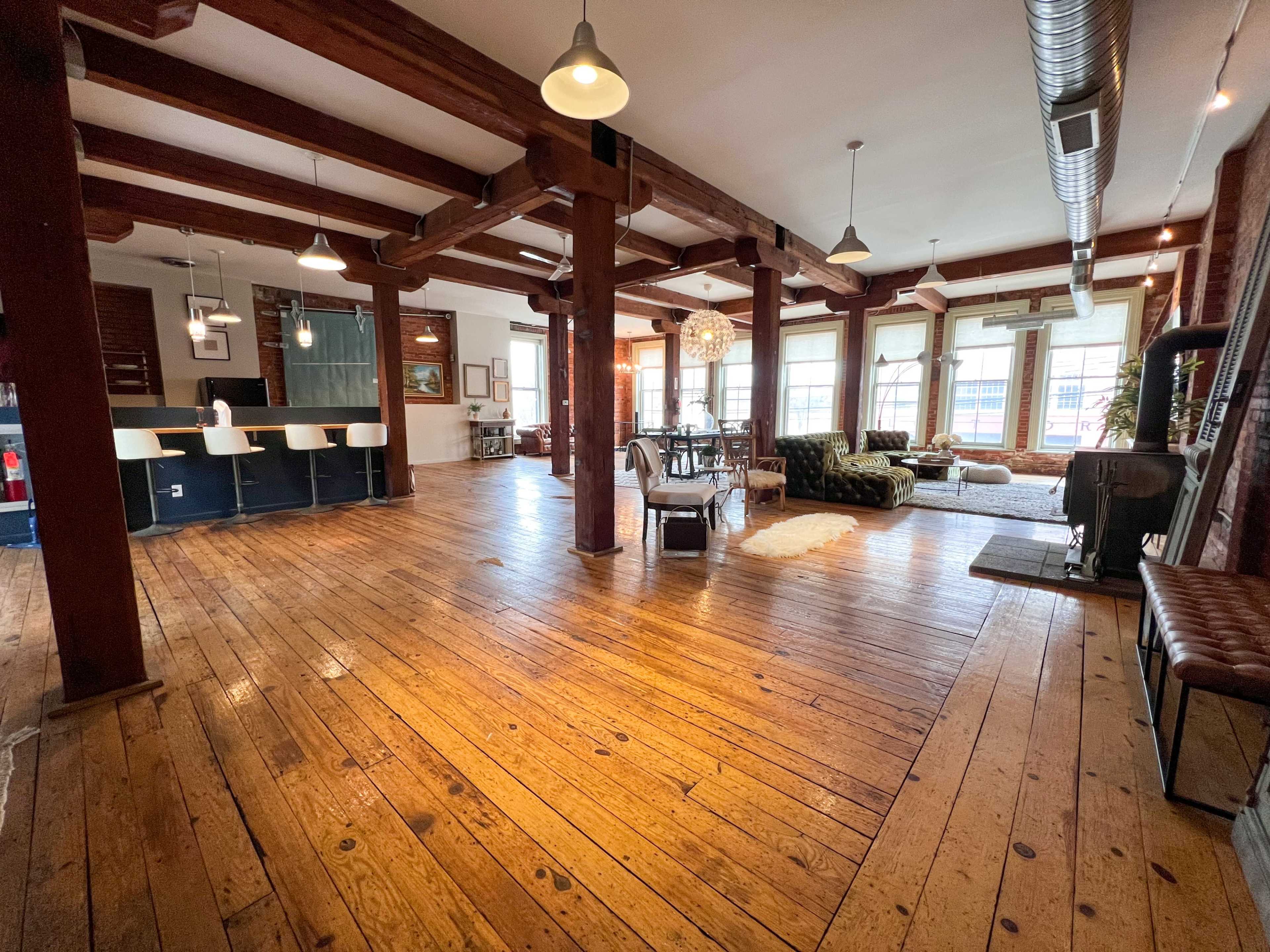 A spacious, open-concept interior with wooden flooring, exposed beams, and a mix of seating areas and dining space.