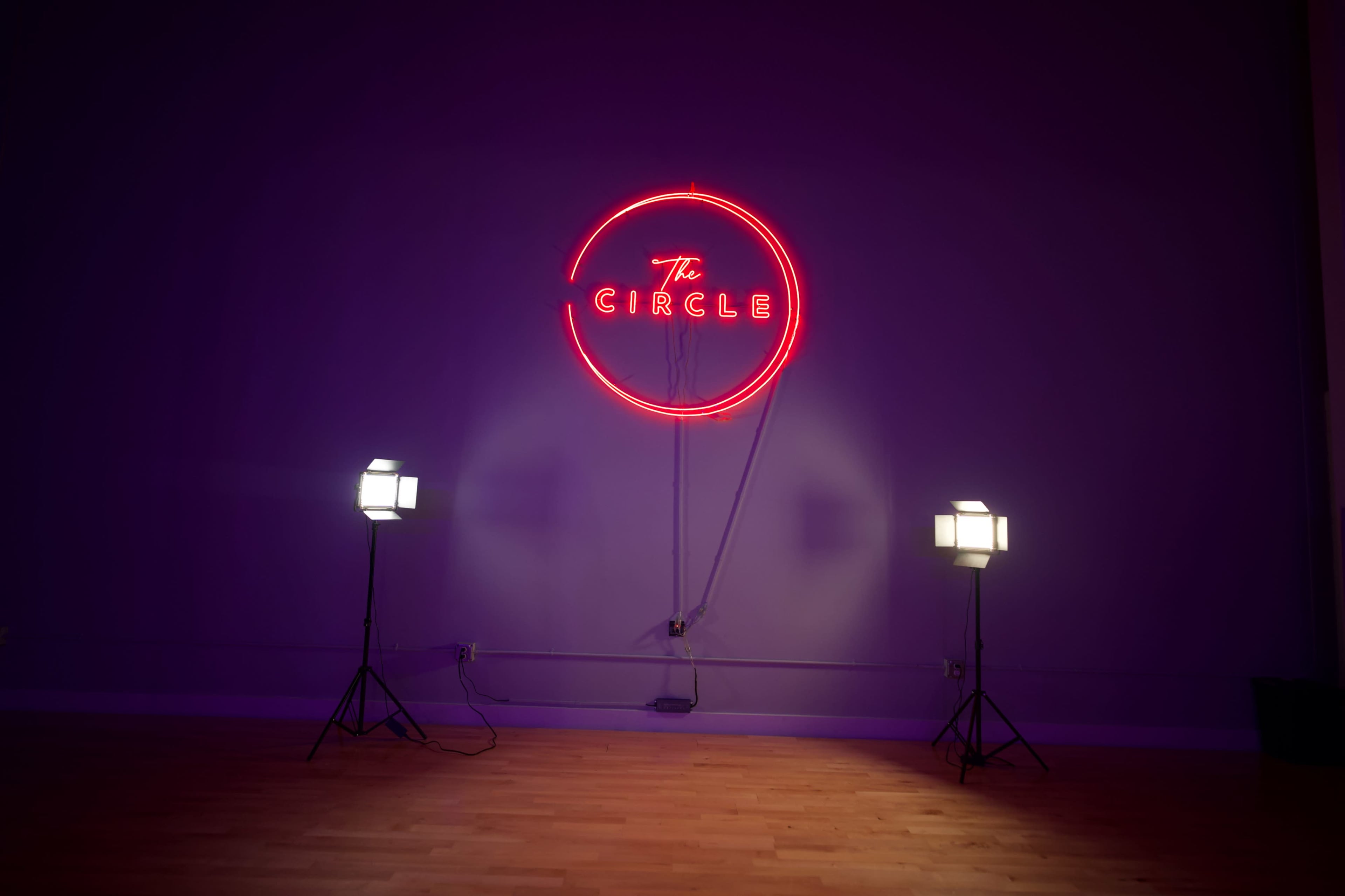 A neon sign reading "The CIRCLE" is mounted on a purple wall, flanked by two studio lights on tripods.