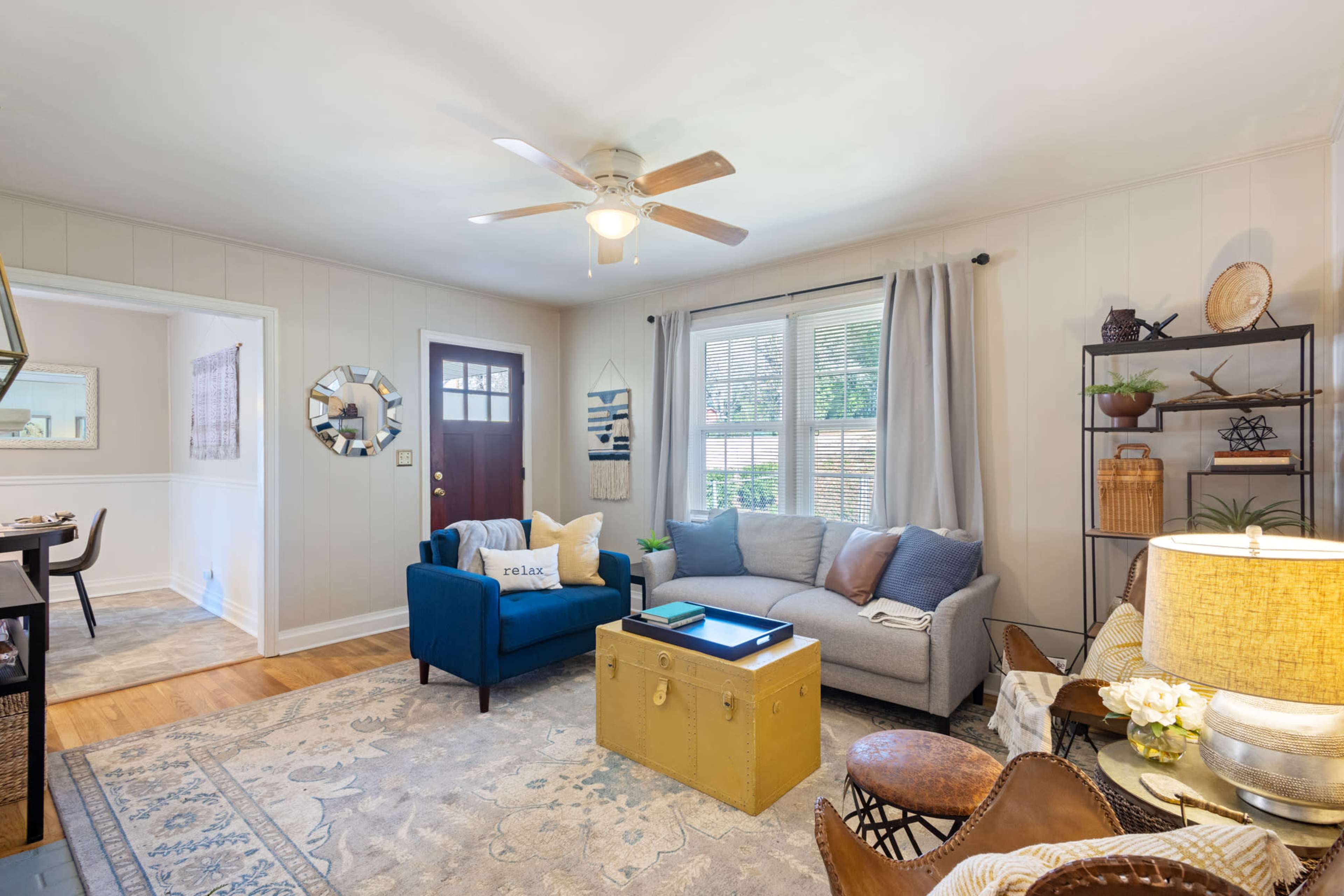 A cozy living room equipped with a grey sofa, a blue armchair, a coffee table, and large windows that allow natural light to illuminate the space.