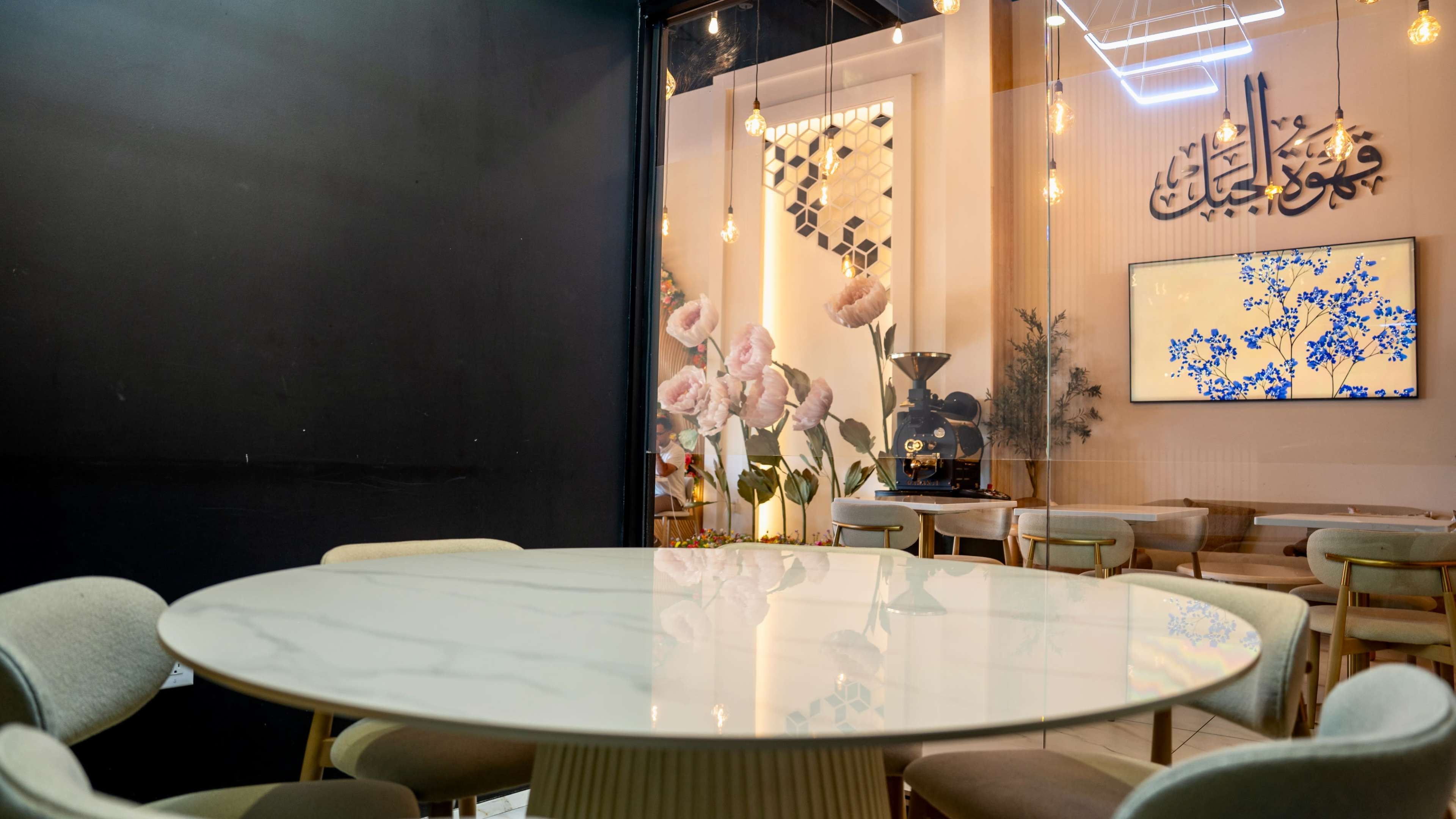 The image shows a modern dining area with a large round marble table surrounded by stylish chairs, alongside a decorative wall featuring floral arrangements and calligraphy art.