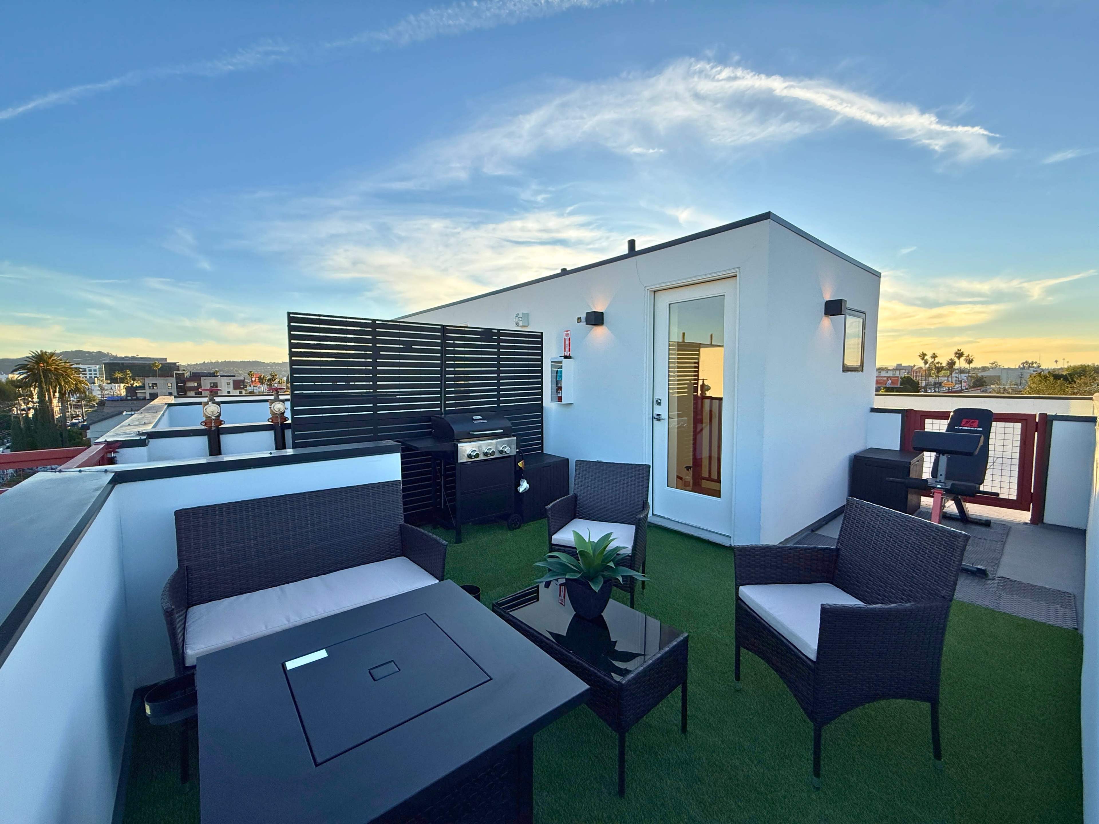 The image shows a rooftop terrace with outdoor seating, a grill, and a clear sky at sunset.