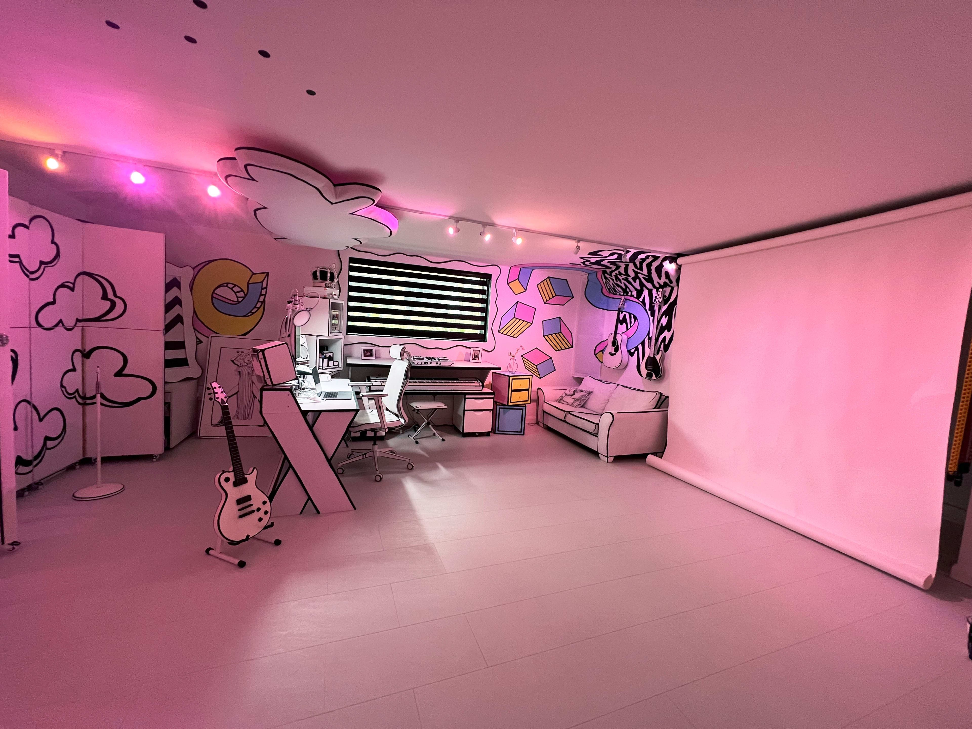The room features a colorful, hand-drawn mural on the walls, with a workspace, a sofa, and a projector screen.