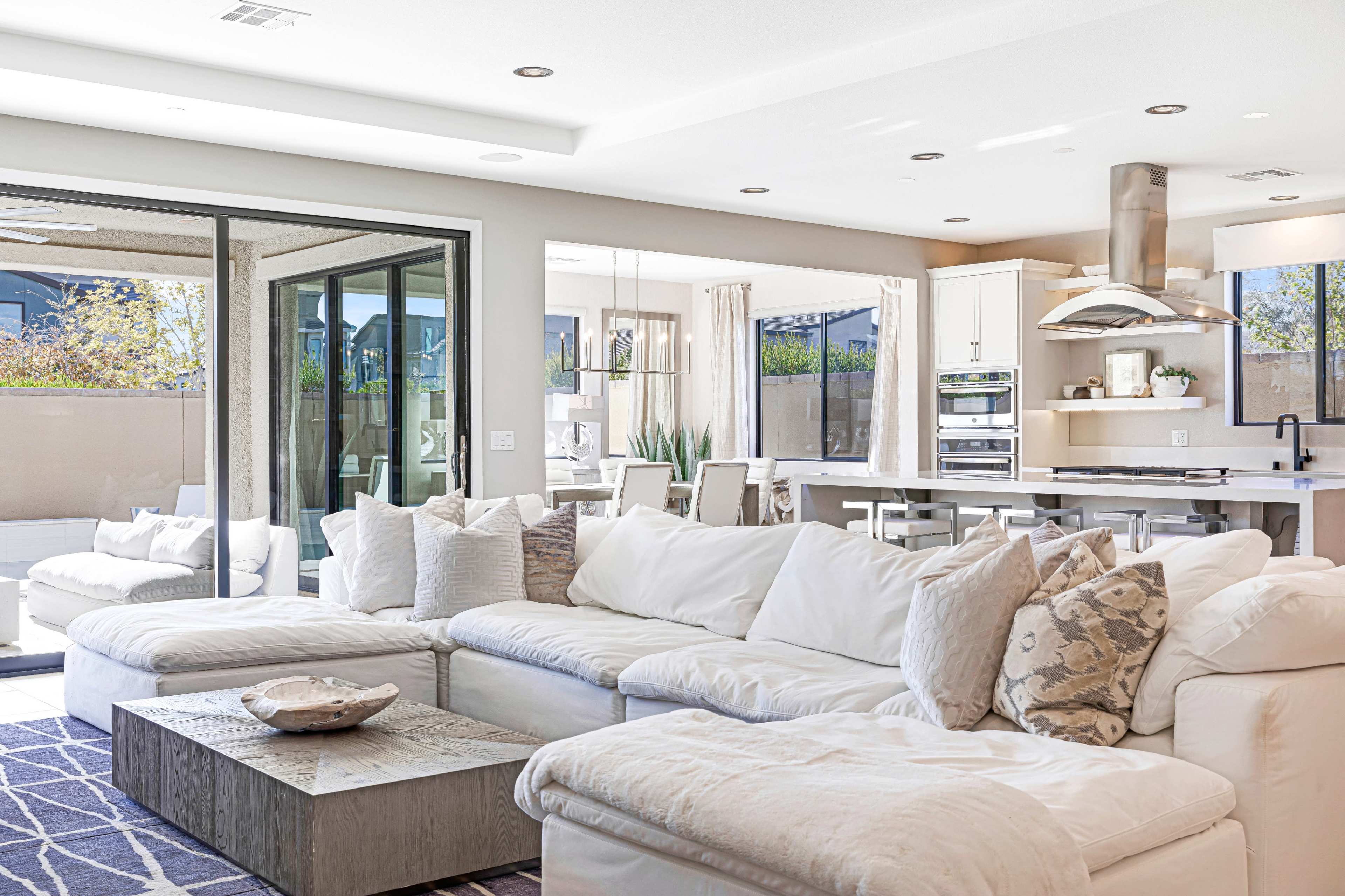 A bright, open-concept living room features a large white sectional sofa and a view of an outdoor patio through sliding glass doors.