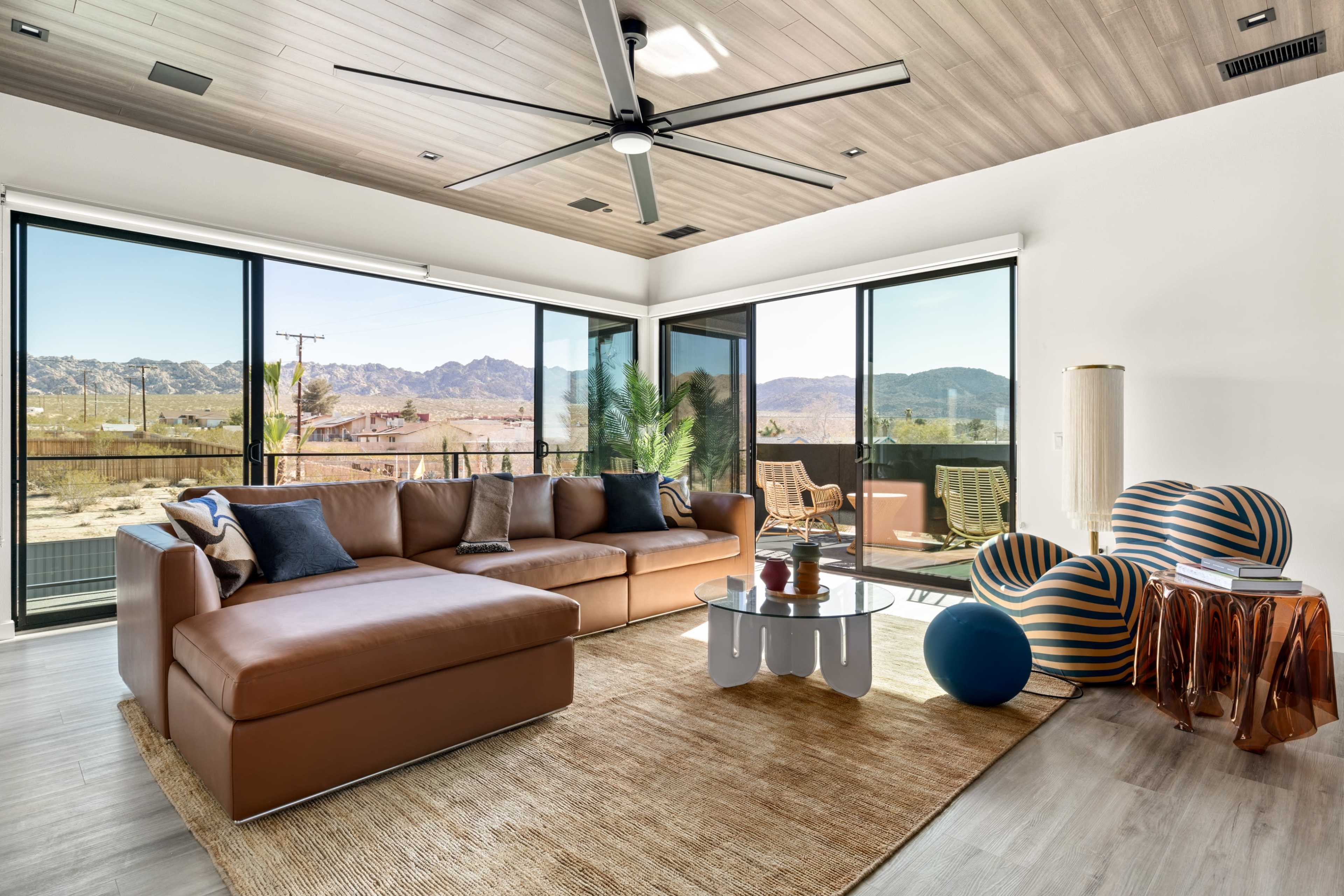 A modern living room features a brown sectional sofa, a round coffee table, and large windows showcasing a mountainous landscape.