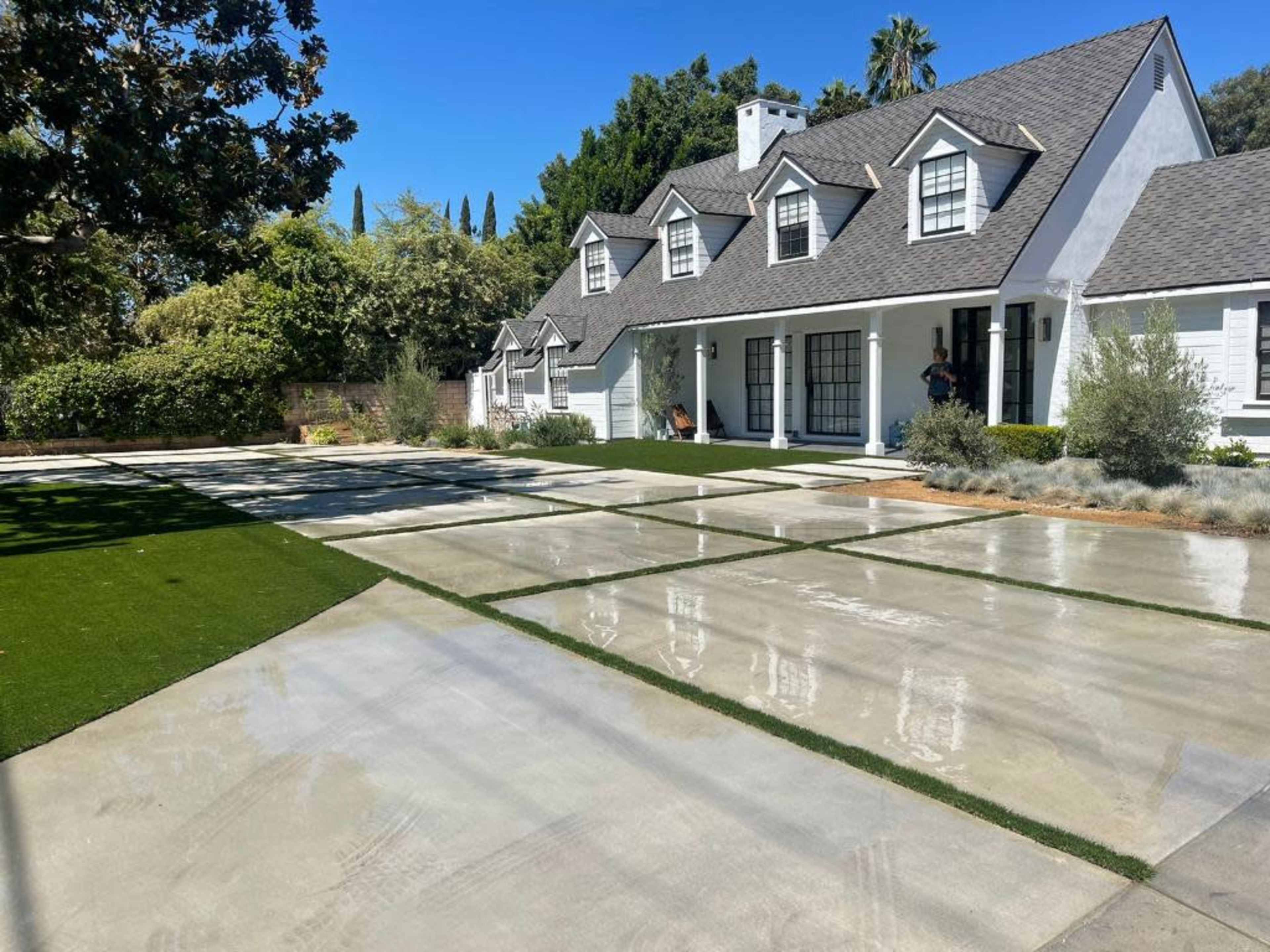 A modern house with a gray roof and white facade is surrounded by manicured lawns and a paved driveway.
