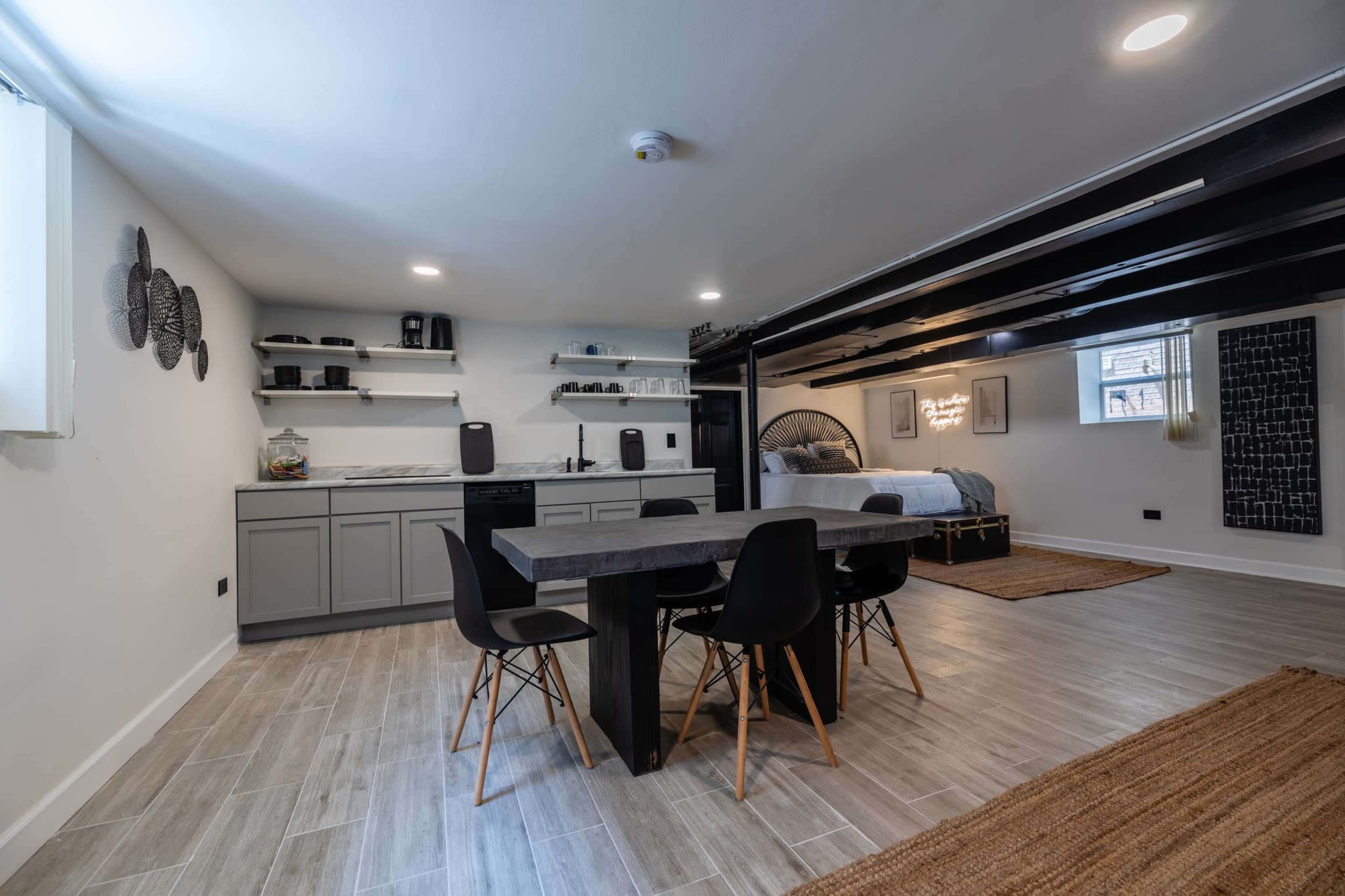 A modern open-concept living space with a kitchenette and dining area featuring a table and chairs, alongside a bed area separated by a railing.