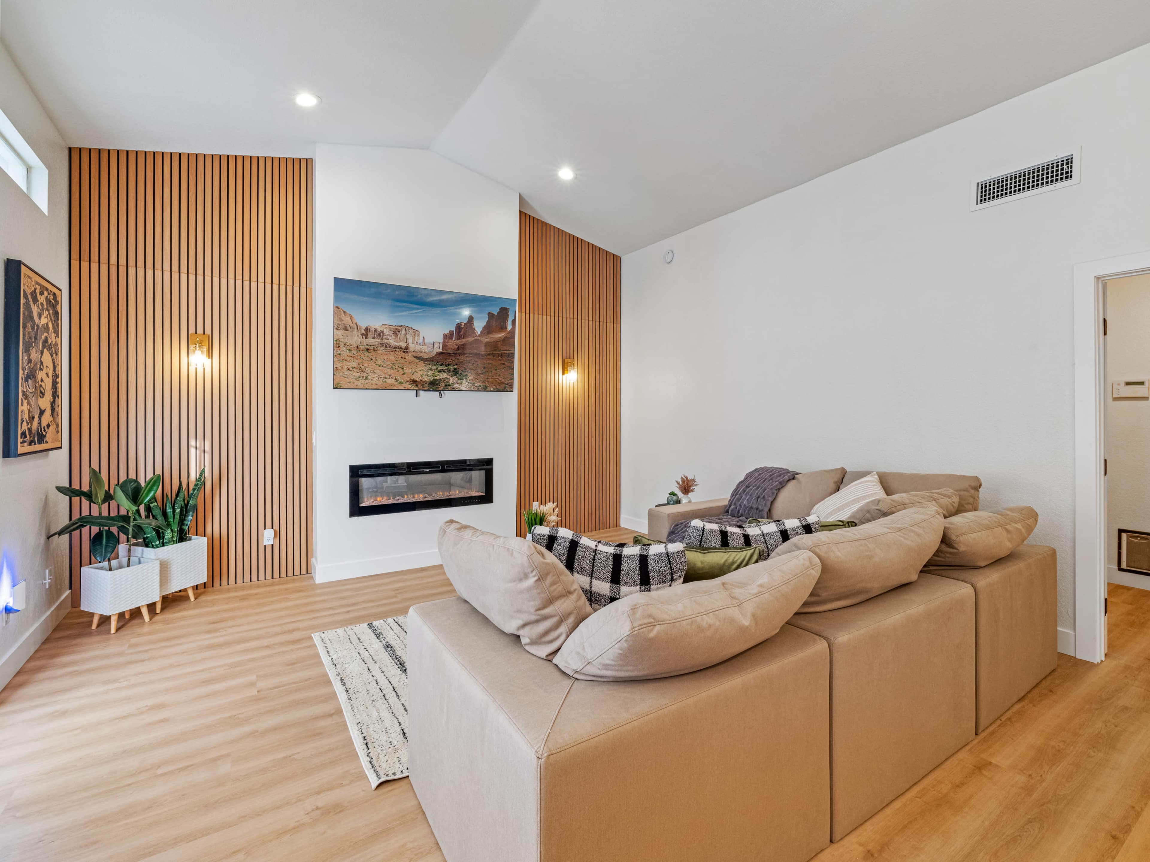 A modern living room with a sectional sofa, a mounted television, and wooden paneling on one wall.