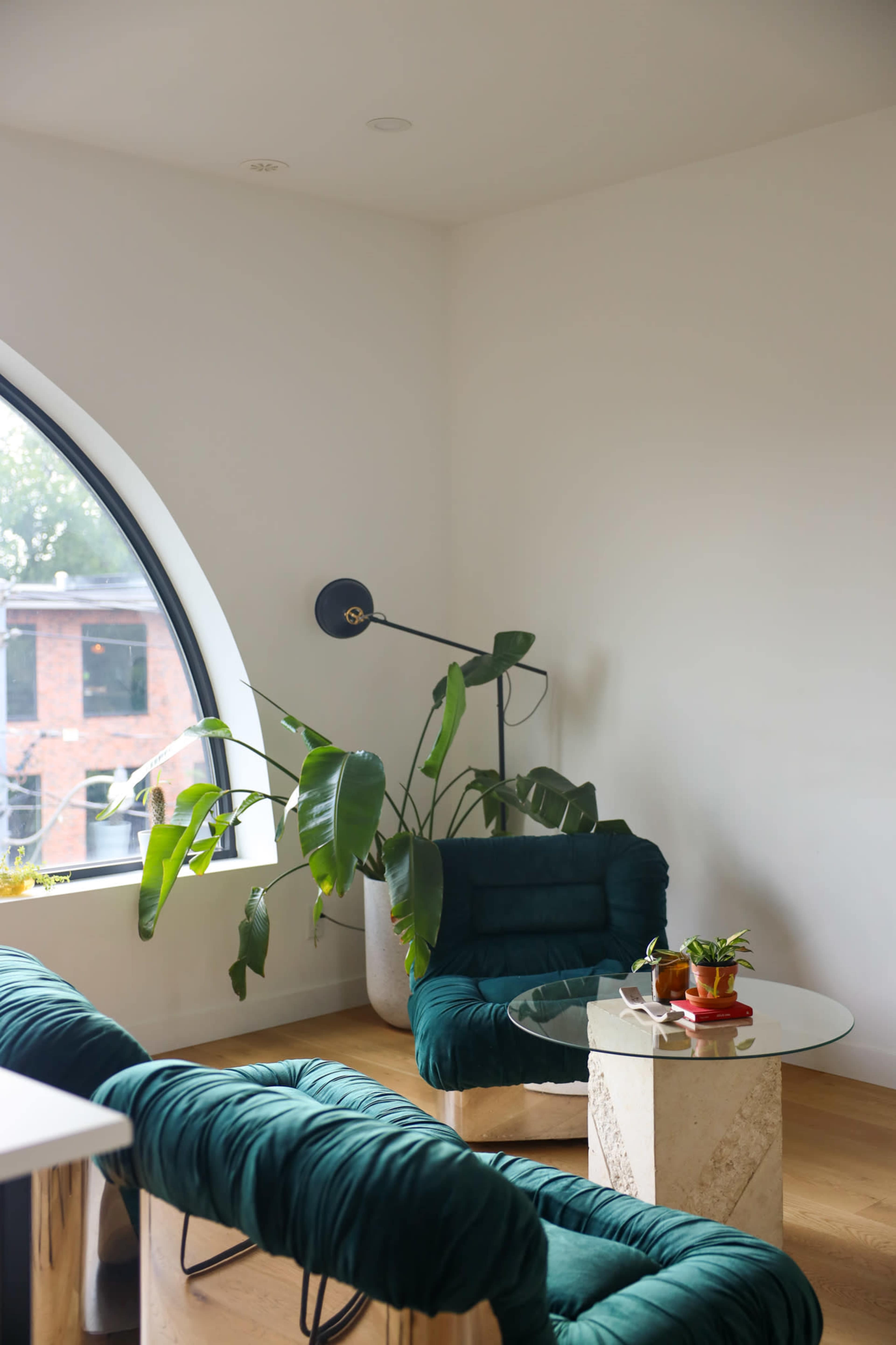 A cozy sitting area features a circular window, a green armchair, a glass table, and a tall plant in a pot.