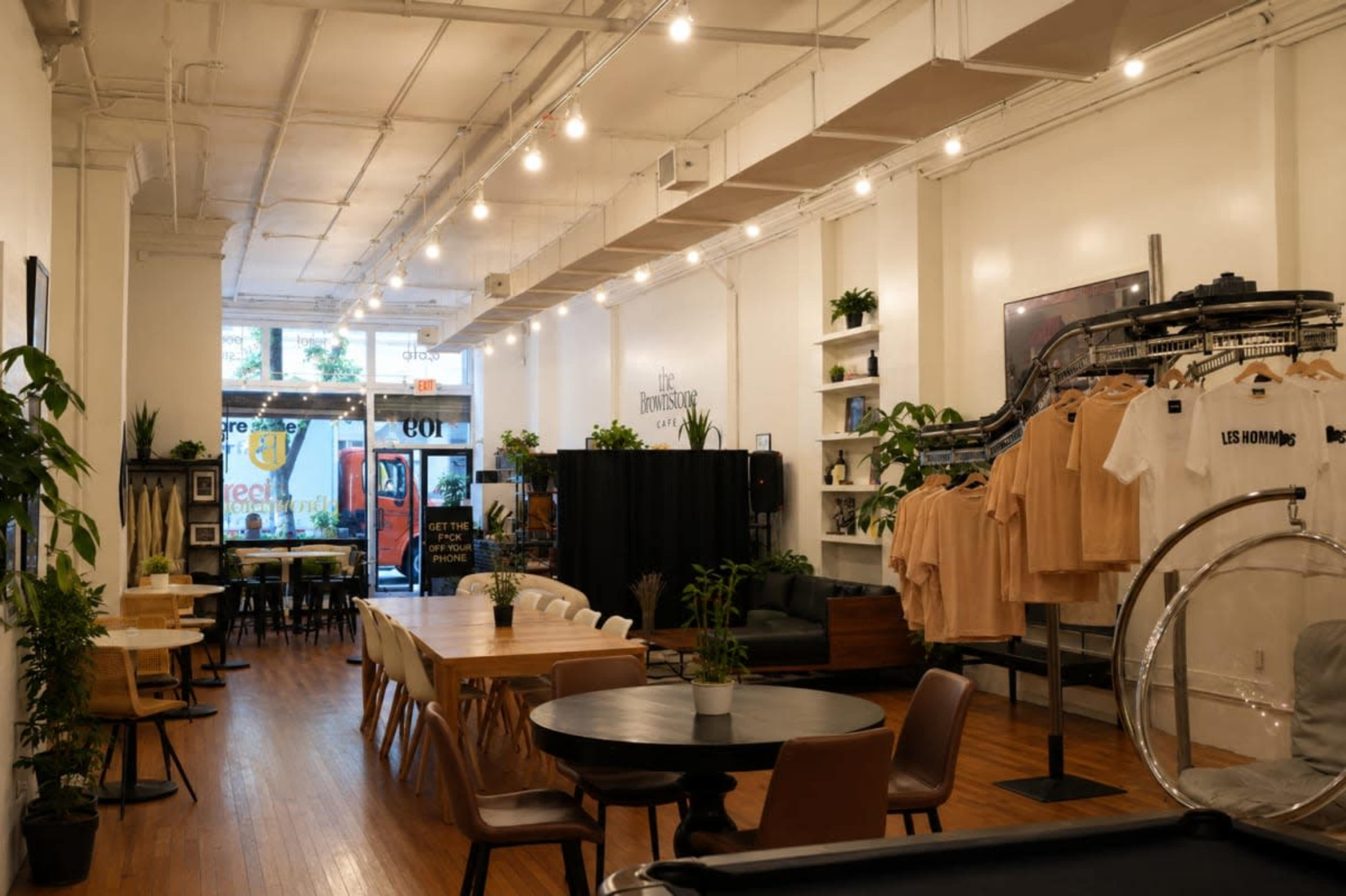 The image shows the interior of a boutique with a mix of seating areas, clothing displays on racks, and large windows revealing an outdoor view.