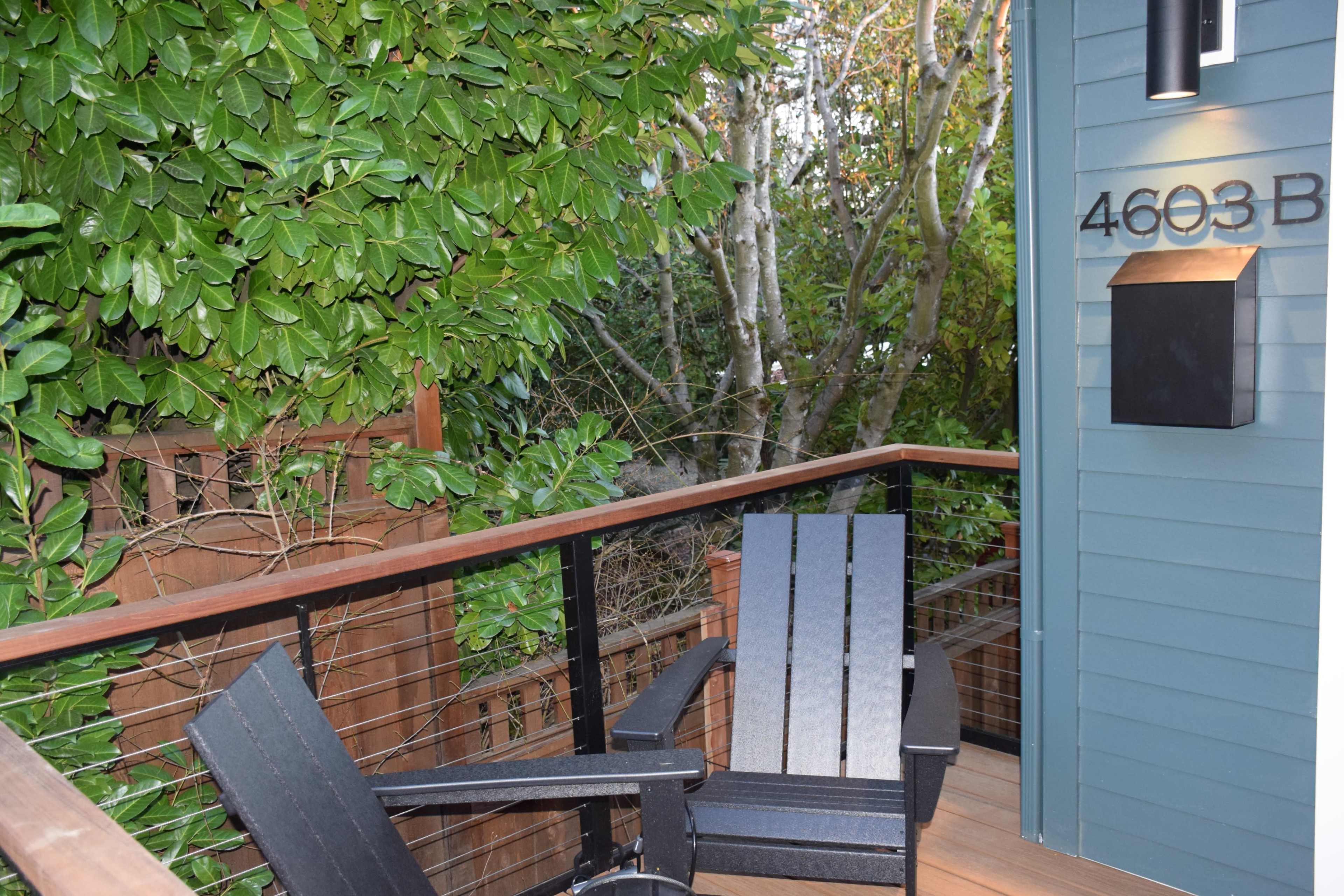 A small outdoor seating area features two black adirondack chairs and a house number sign mounted on the wall beside a mailbox.