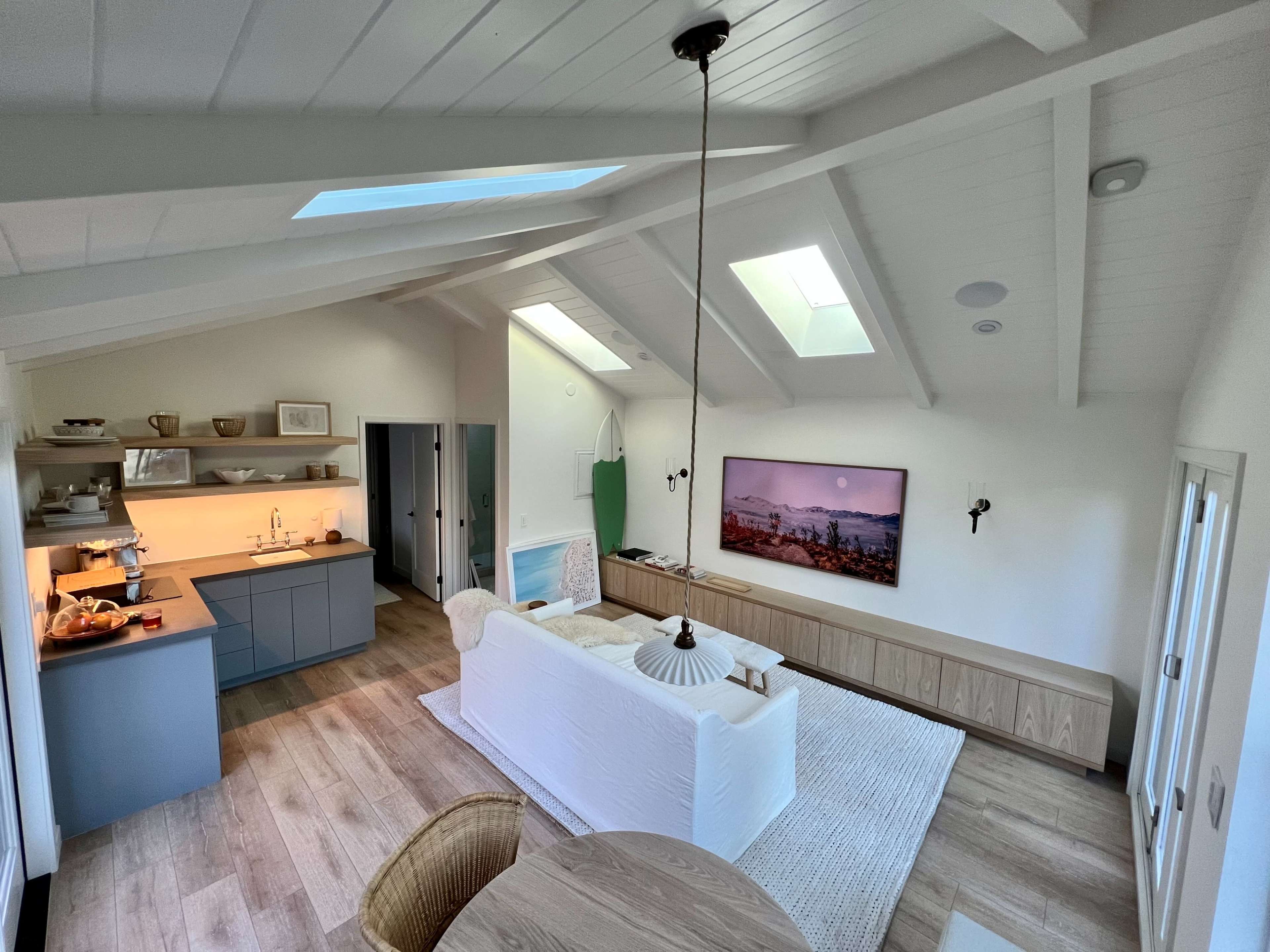 A modern, open-concept living space with a light wooden floor, skylights, and a cozy seating area featuring a white sofa and a wooden entertainment unit.