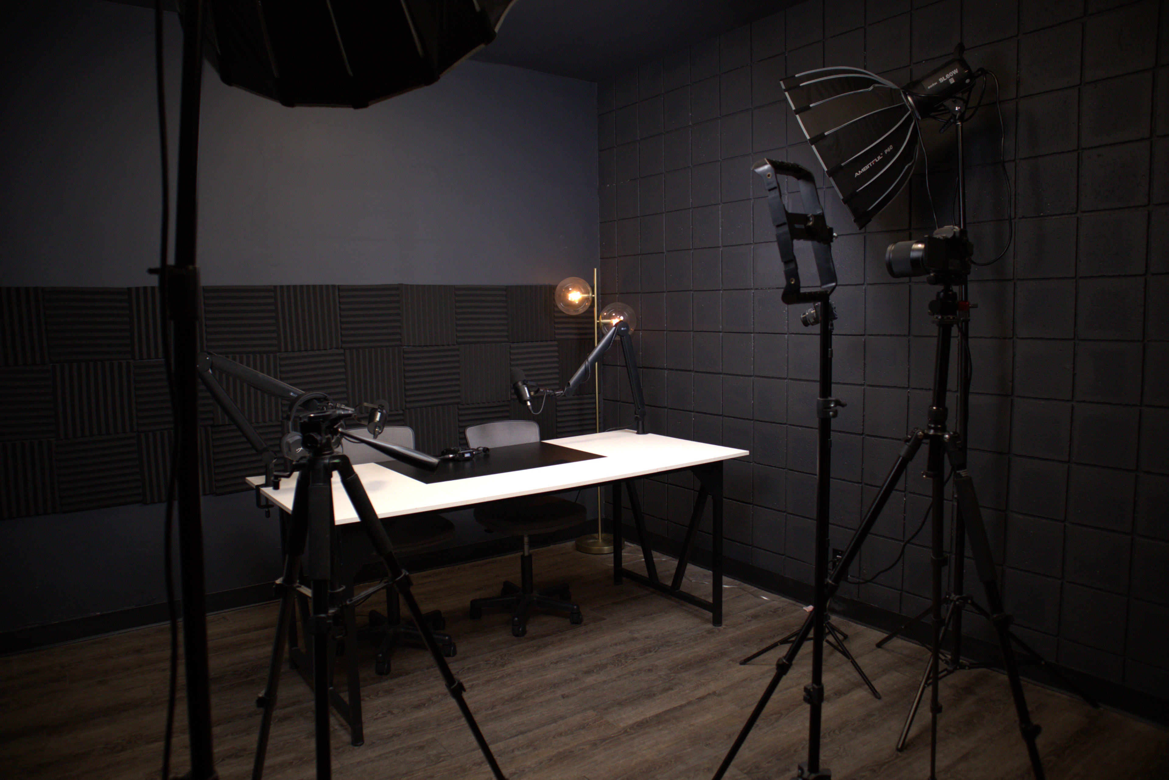 A minimalistic recording studio featuring a desk and chair surrounded by studio lights and soundproofing panels on the walls.