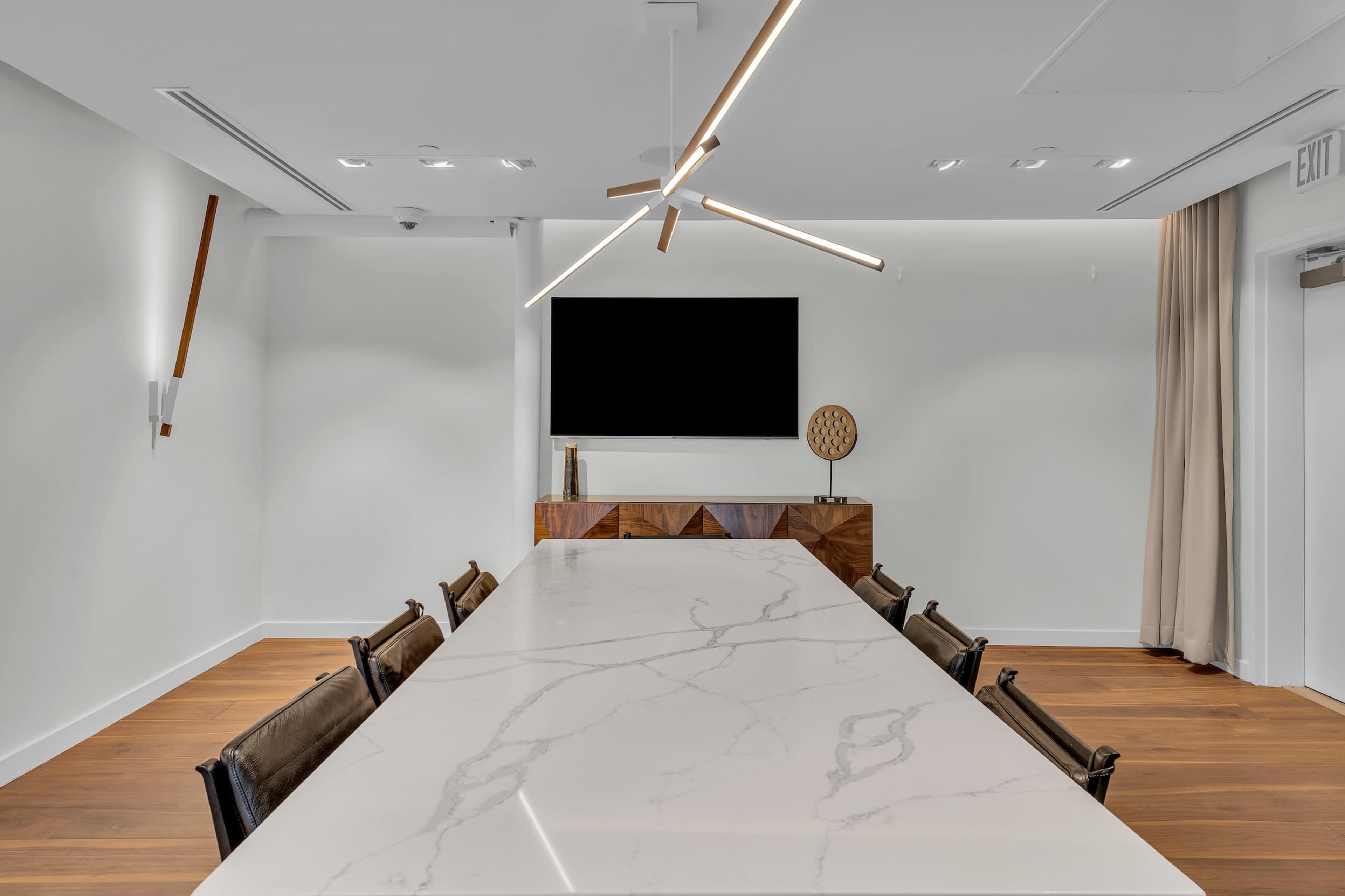 A modern conference room features a long marble table, a wall-mounted television, and minimalist wooden accents.