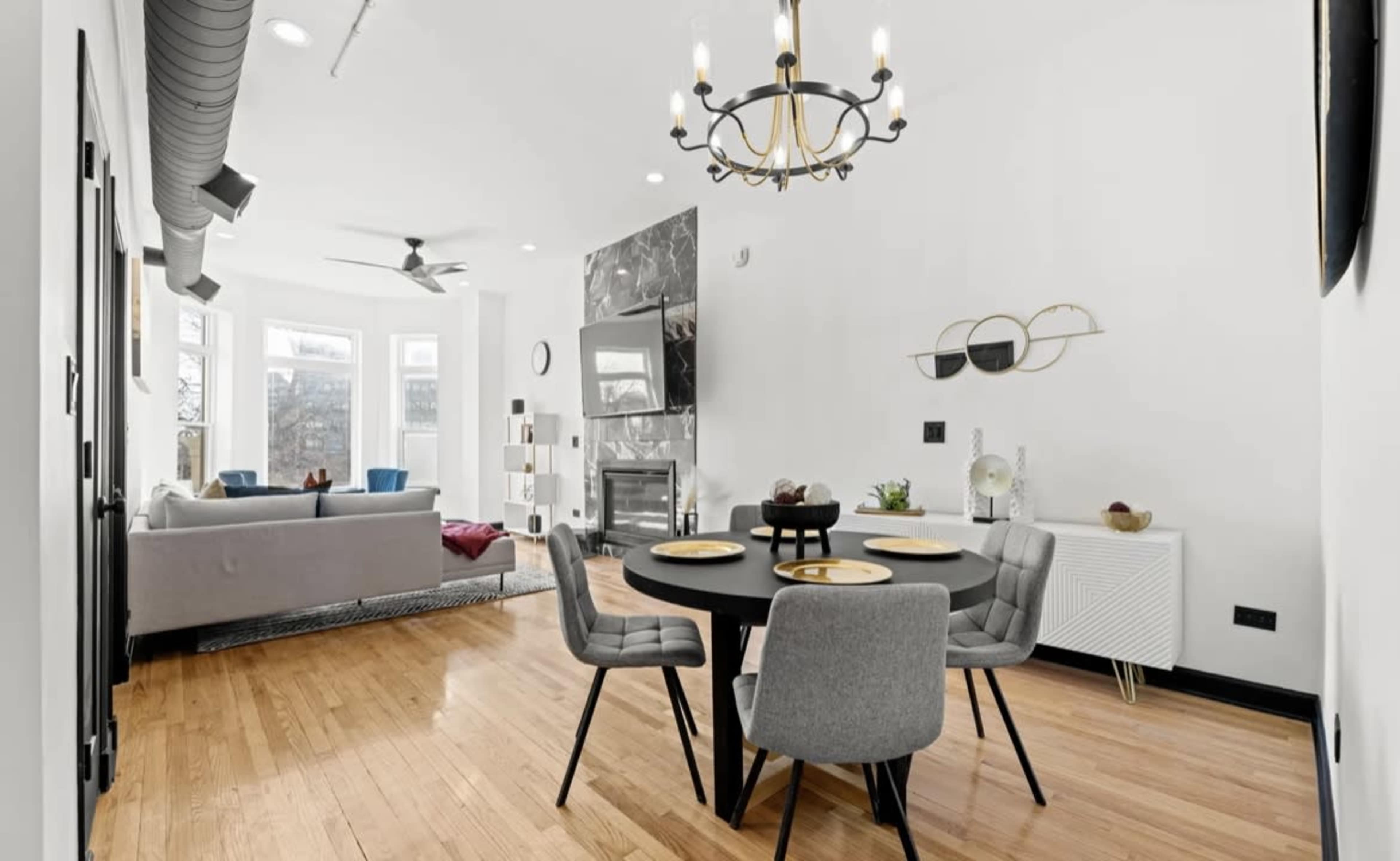 A modern dining area with a round black table and gray chairs, adjacent to a cozy living room featuring a gray sofa and a fireplace.