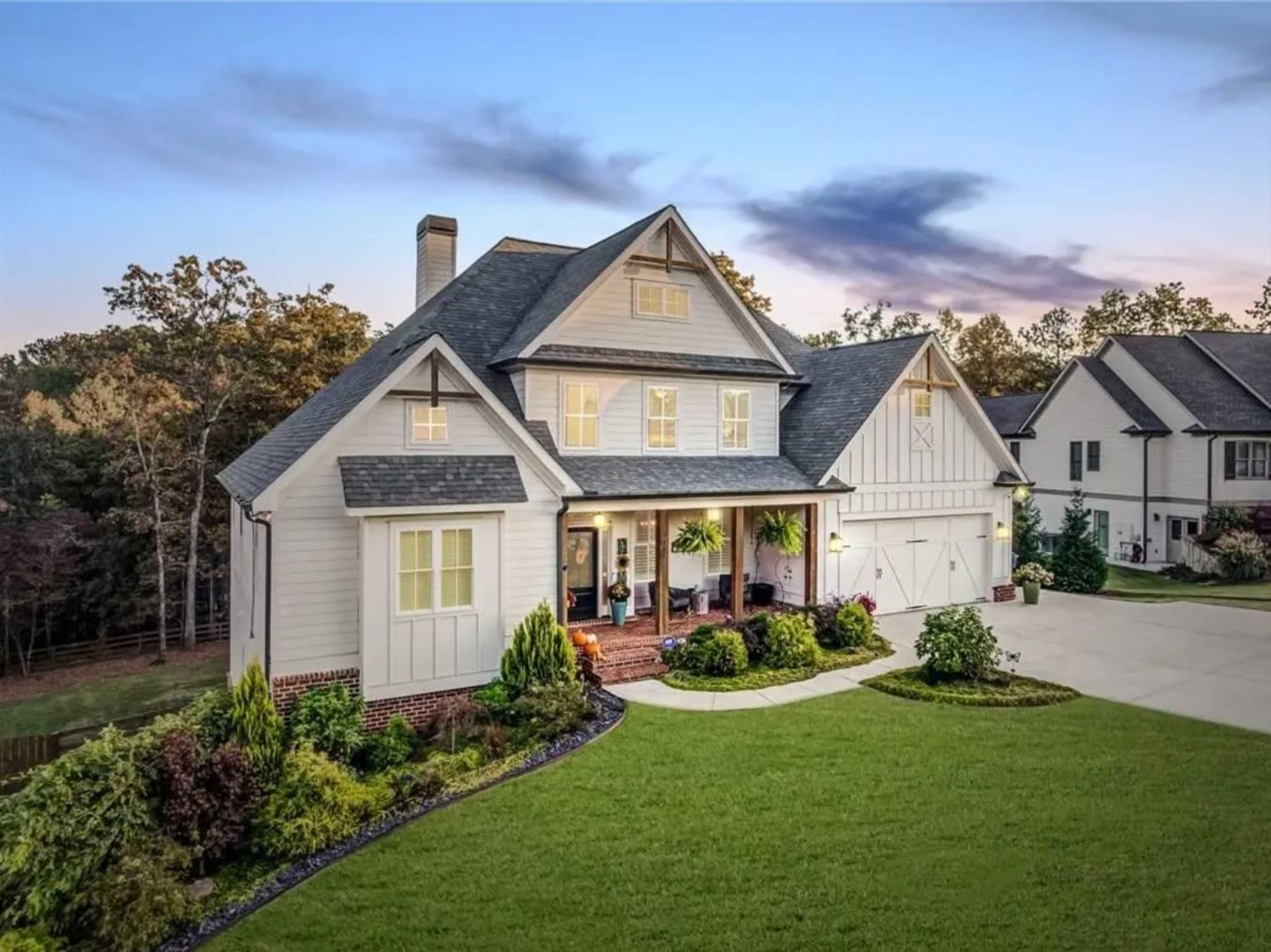 A modern two-story house with a gray roof and white exterior is surrounded by a well-maintained lawn and garden.