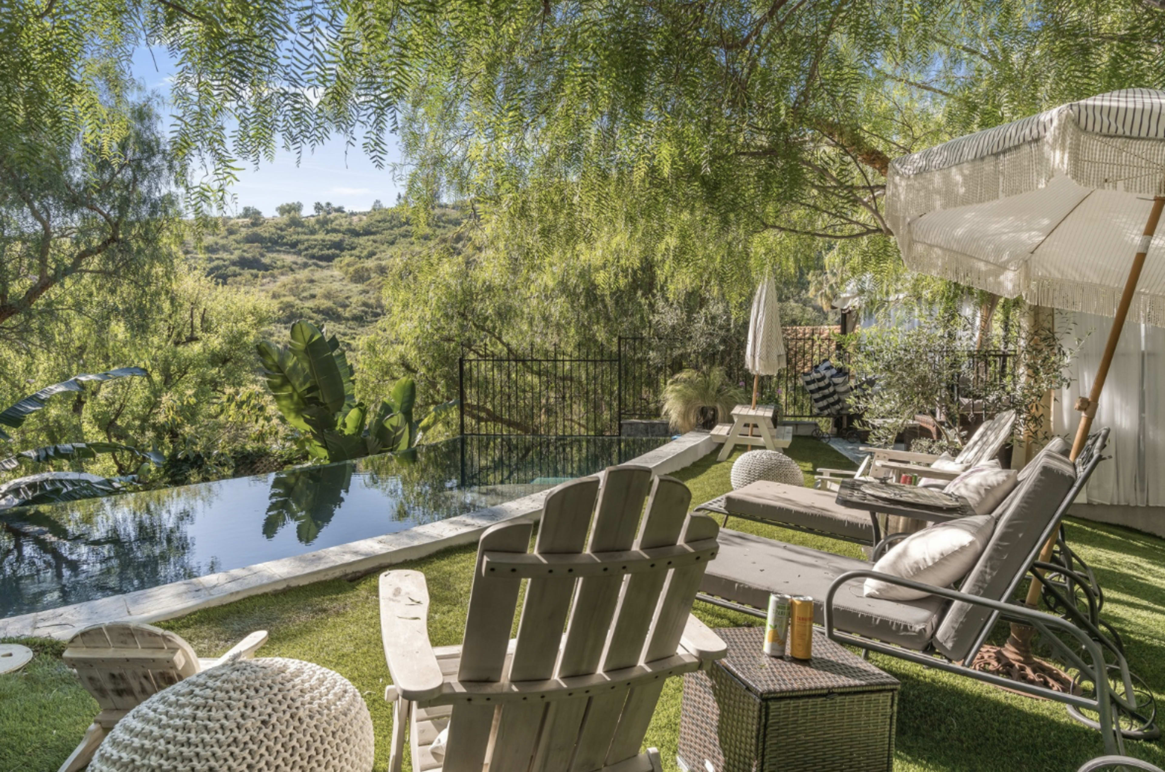 The image depicts a serene outdoor space with a swimming pool surrounded by lounge chairs and lush greenery.