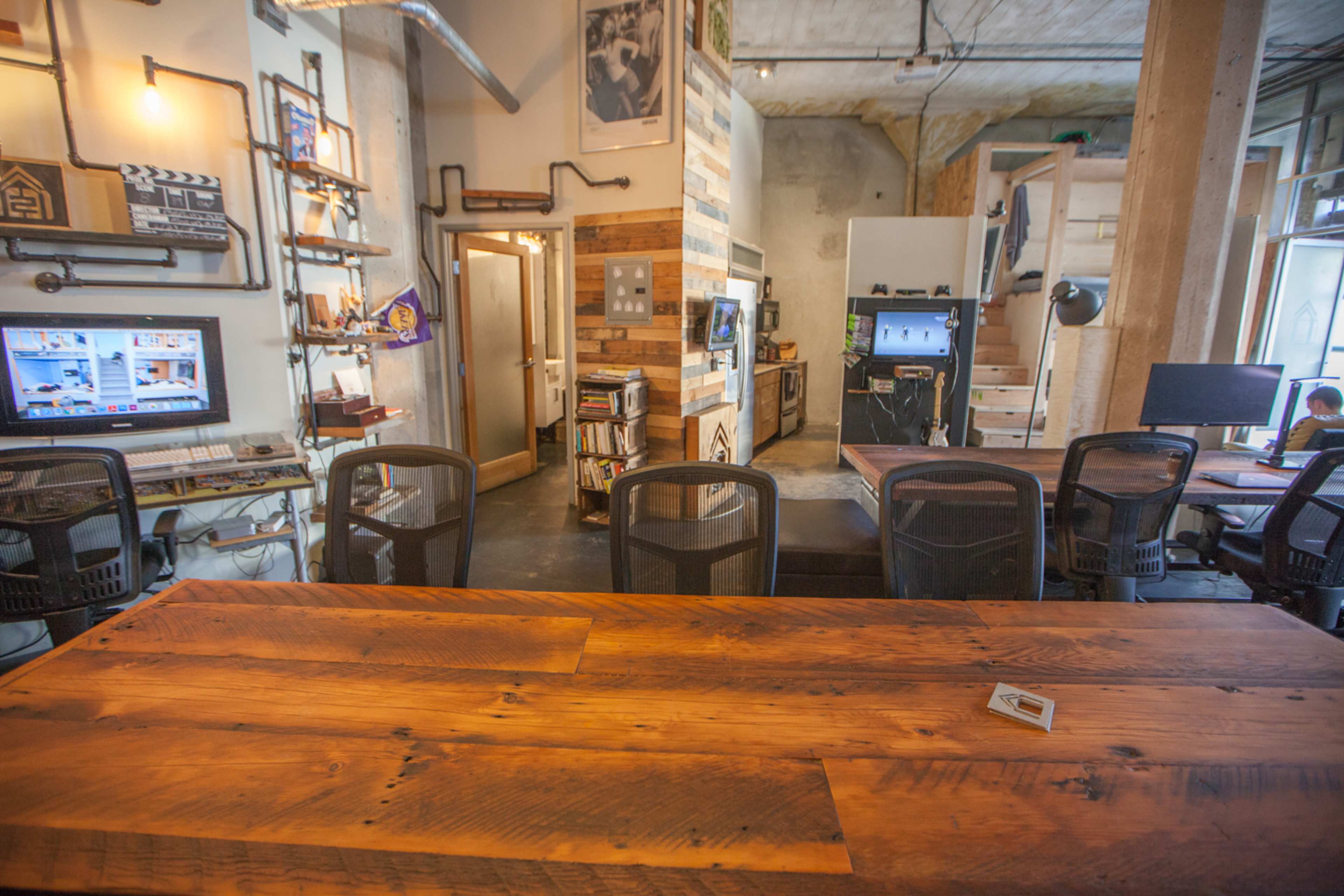 A modern office space featuring wooden tables, several computers, and a rustic design with exposed walls.
