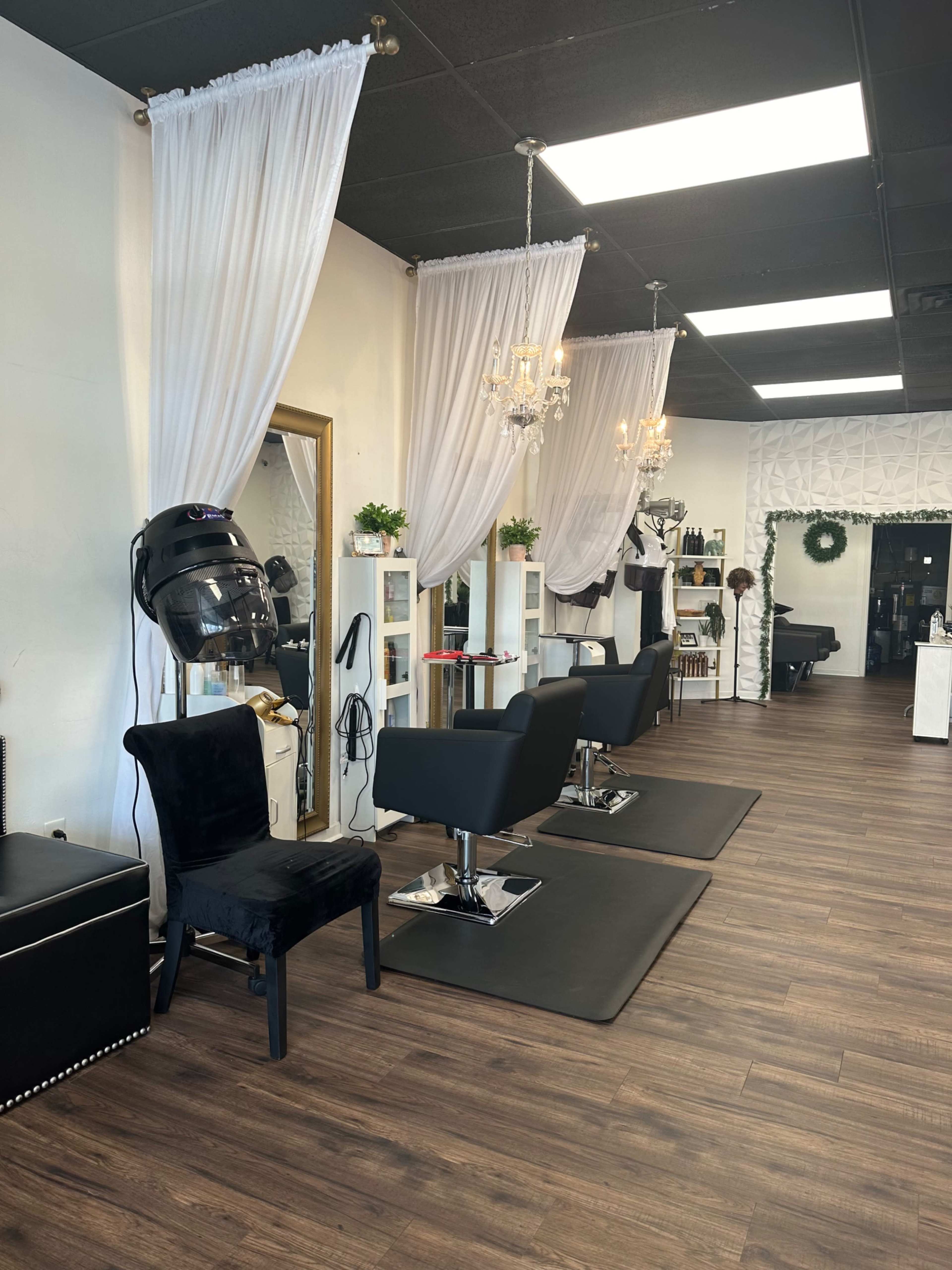 The image shows a modern hair salon with two styling stations separated by white drapes, dark wood flooring, and various salon equipment.