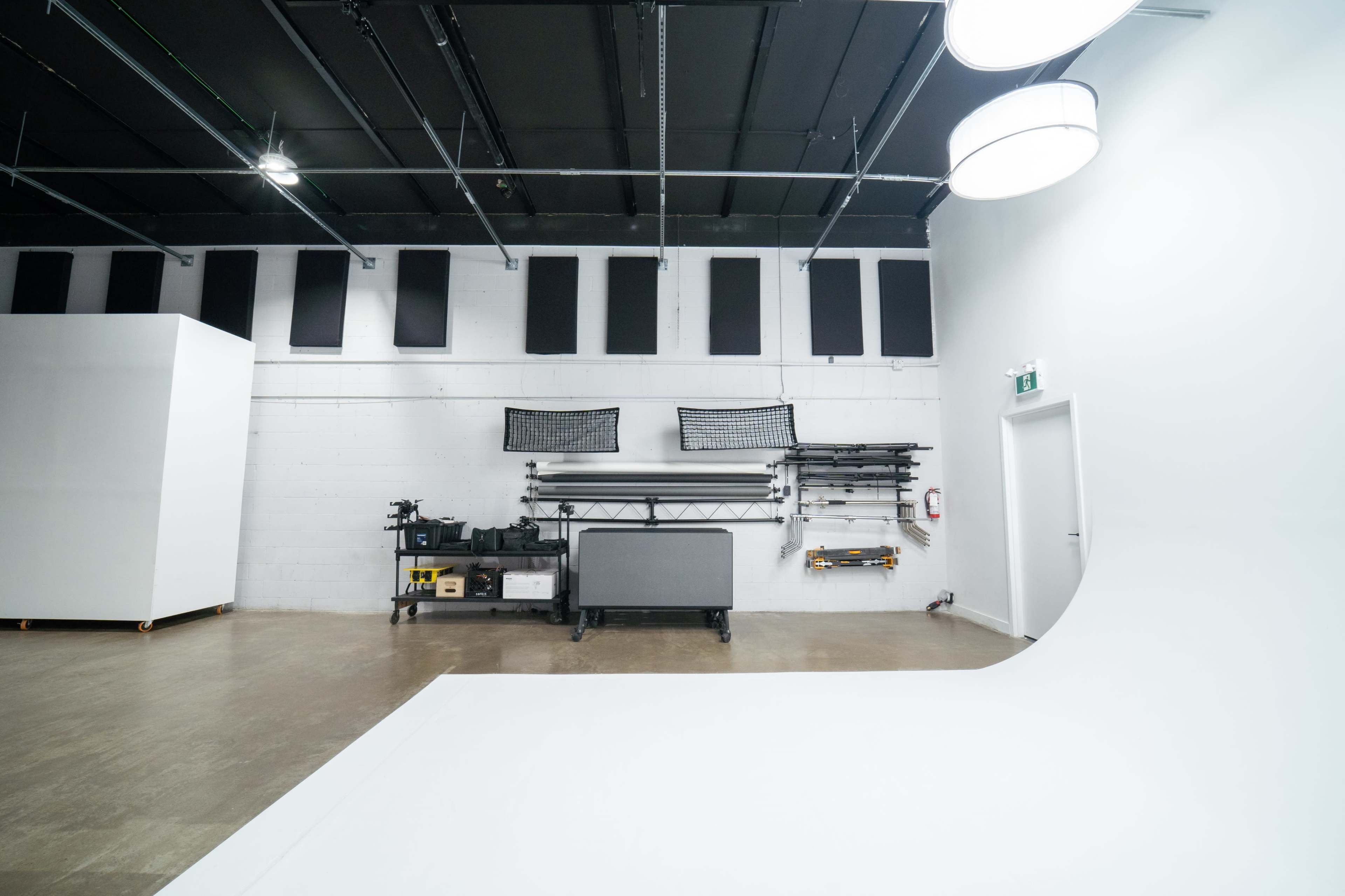 A spacious, brightly lit photography studio featuring a seamless white backdrop, equipment storage, and a minimalistic design.