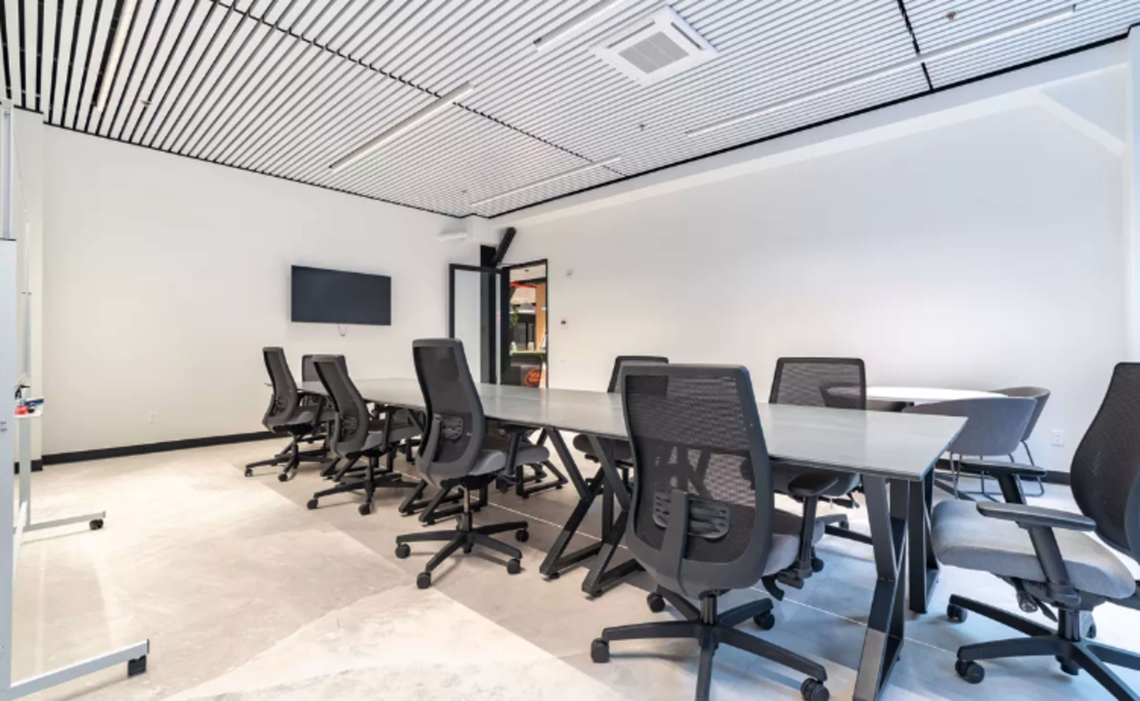 A modern conference room with a long glass table surrounded by black mesh chairs.