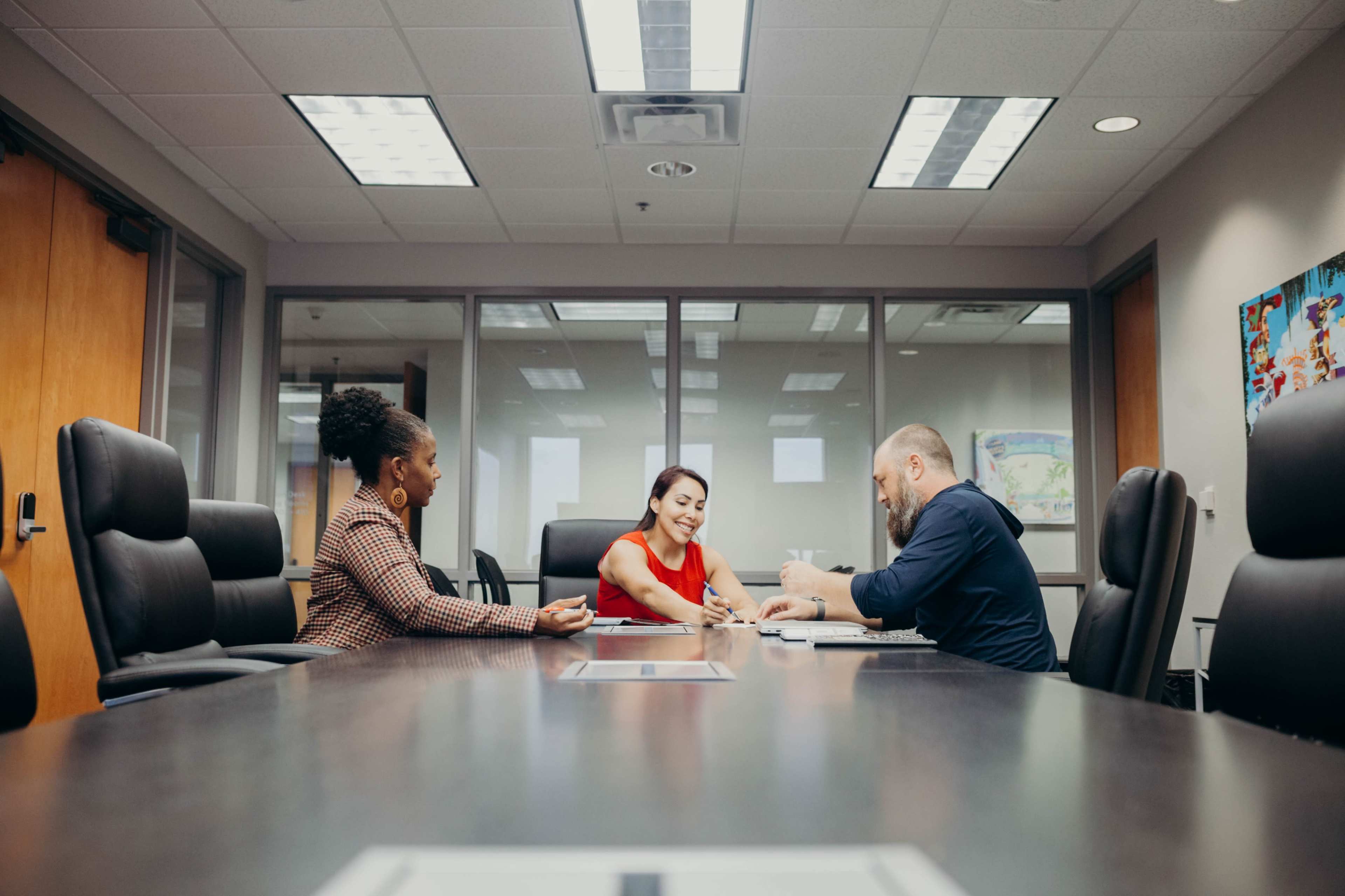 Three colleagues hold a meeting around a conference table in a well-lit office.
