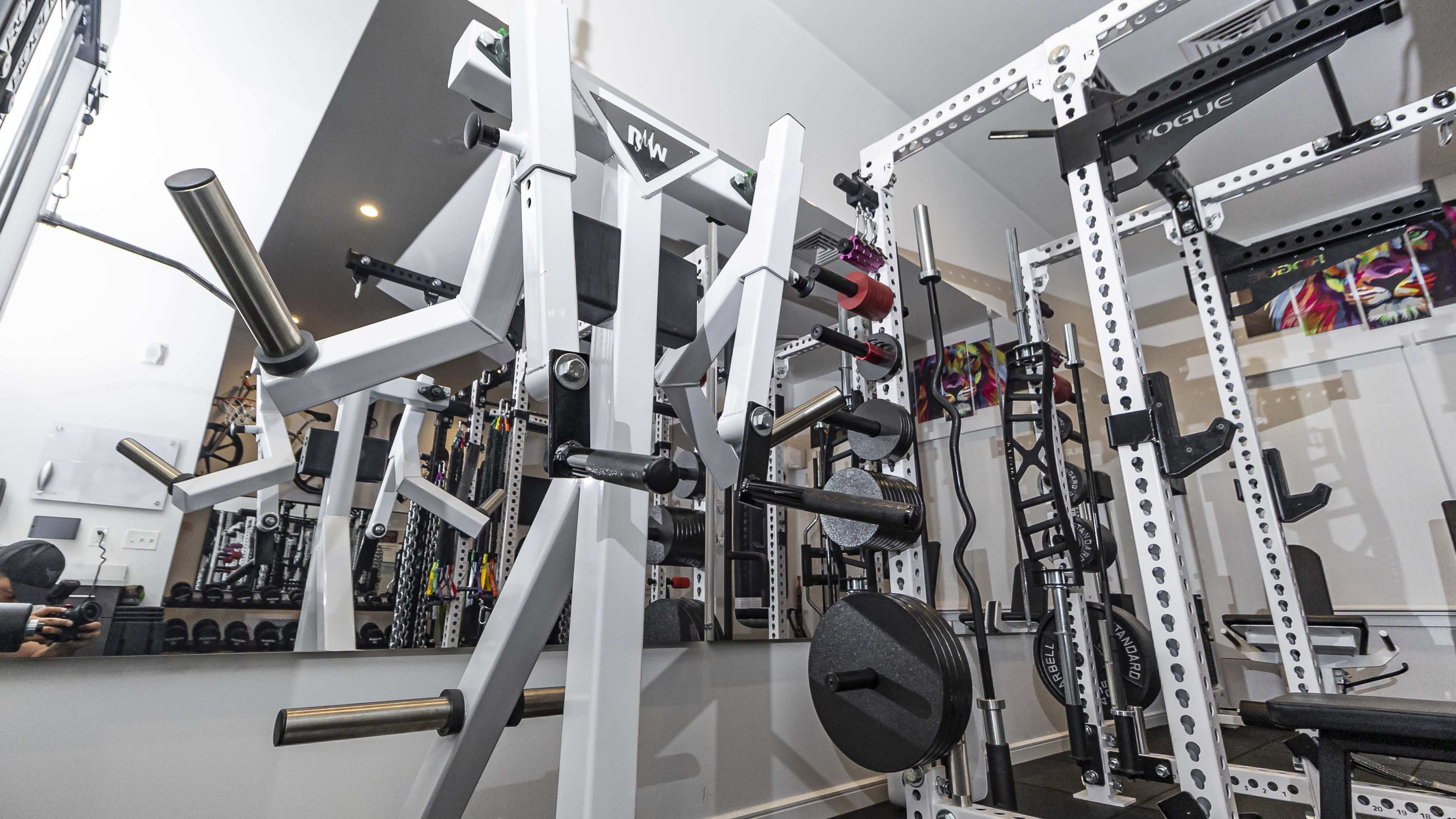 A well-equipped gym space featuring a weight rack, a squat rack, and various weight plates organized on a barbell.