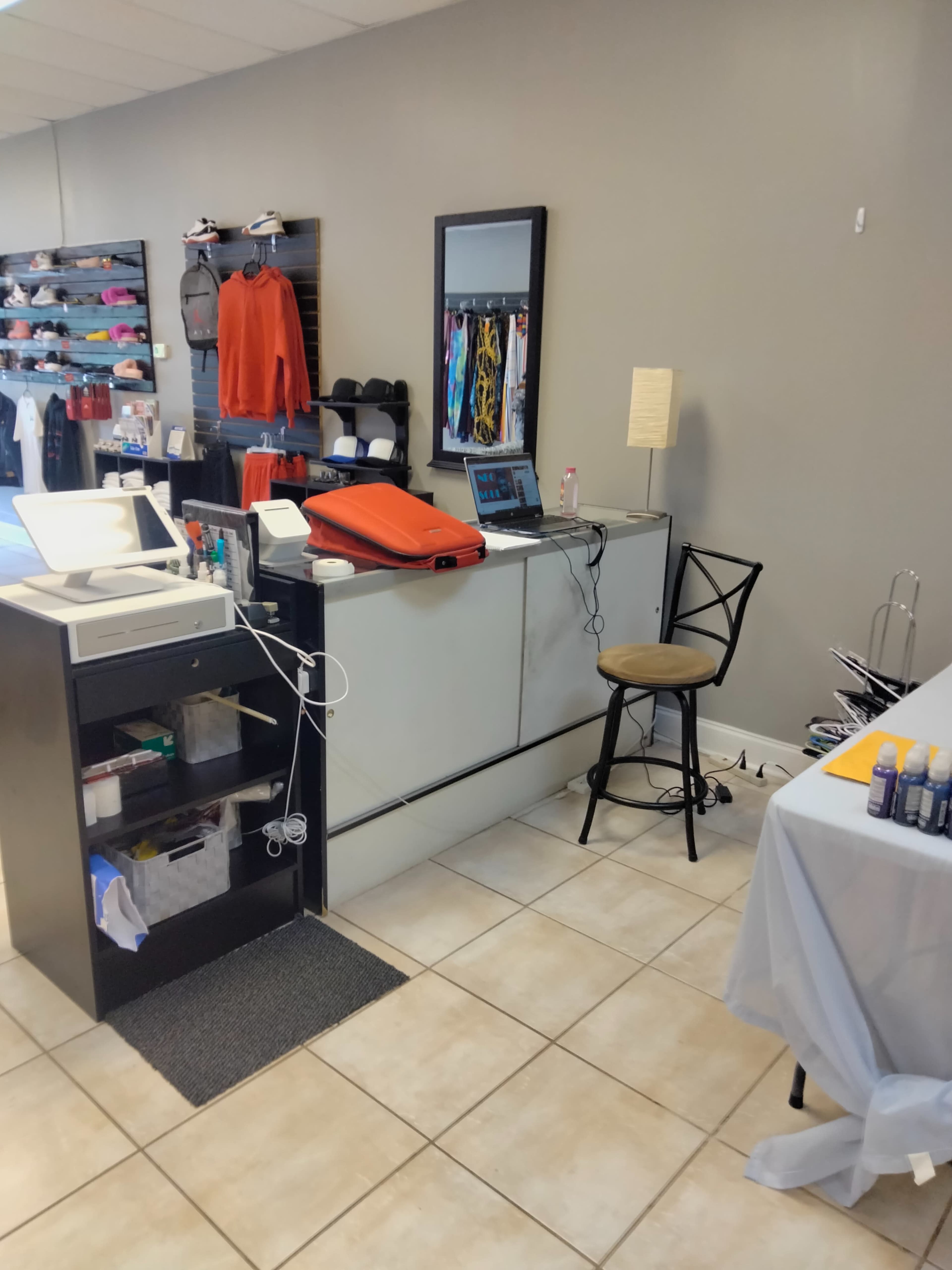 A retail space featuring a payment counter, a computer, a stool, and shelves stocked with clothing items.