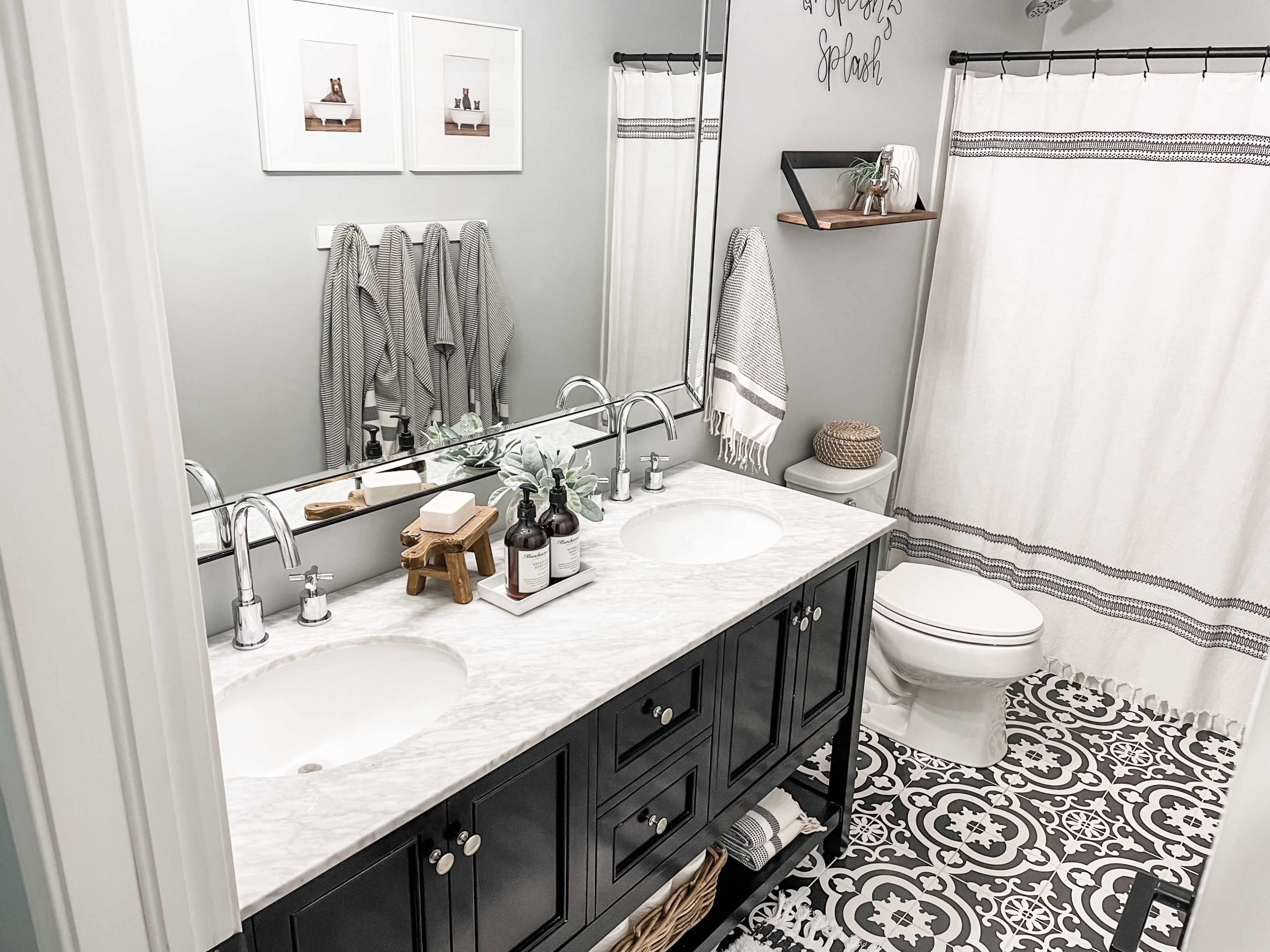 A modern bathroom featuring a double vanity with a marble countertop, a large mirror, gray walls, patterned flooring, and a shower curtain.