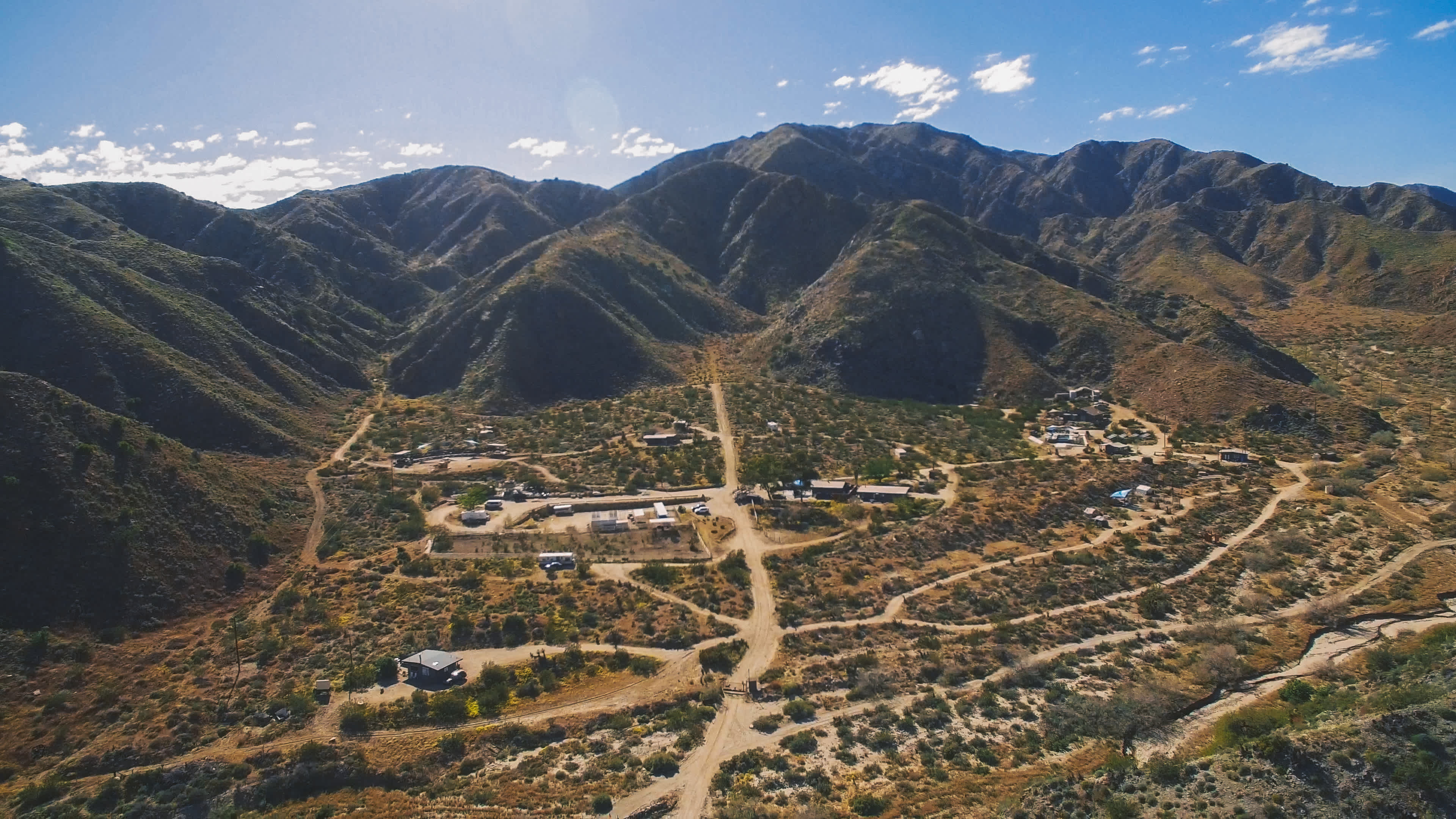 A mountainous landscape with a small settlement and dirt roads winding through arid terrain.