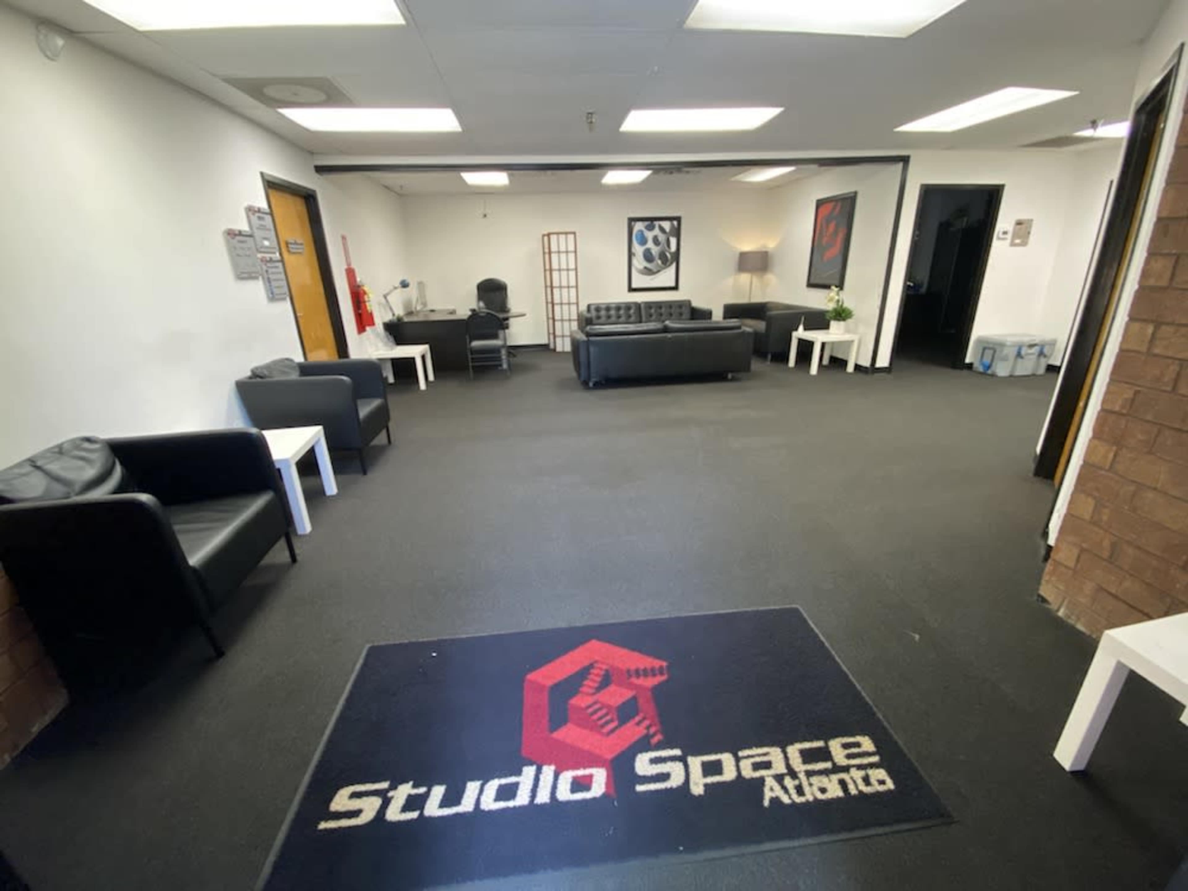 The image shows a spacious waiting area with black leather furniture and a carpet featuring the logo "Studio Space Atlanta."