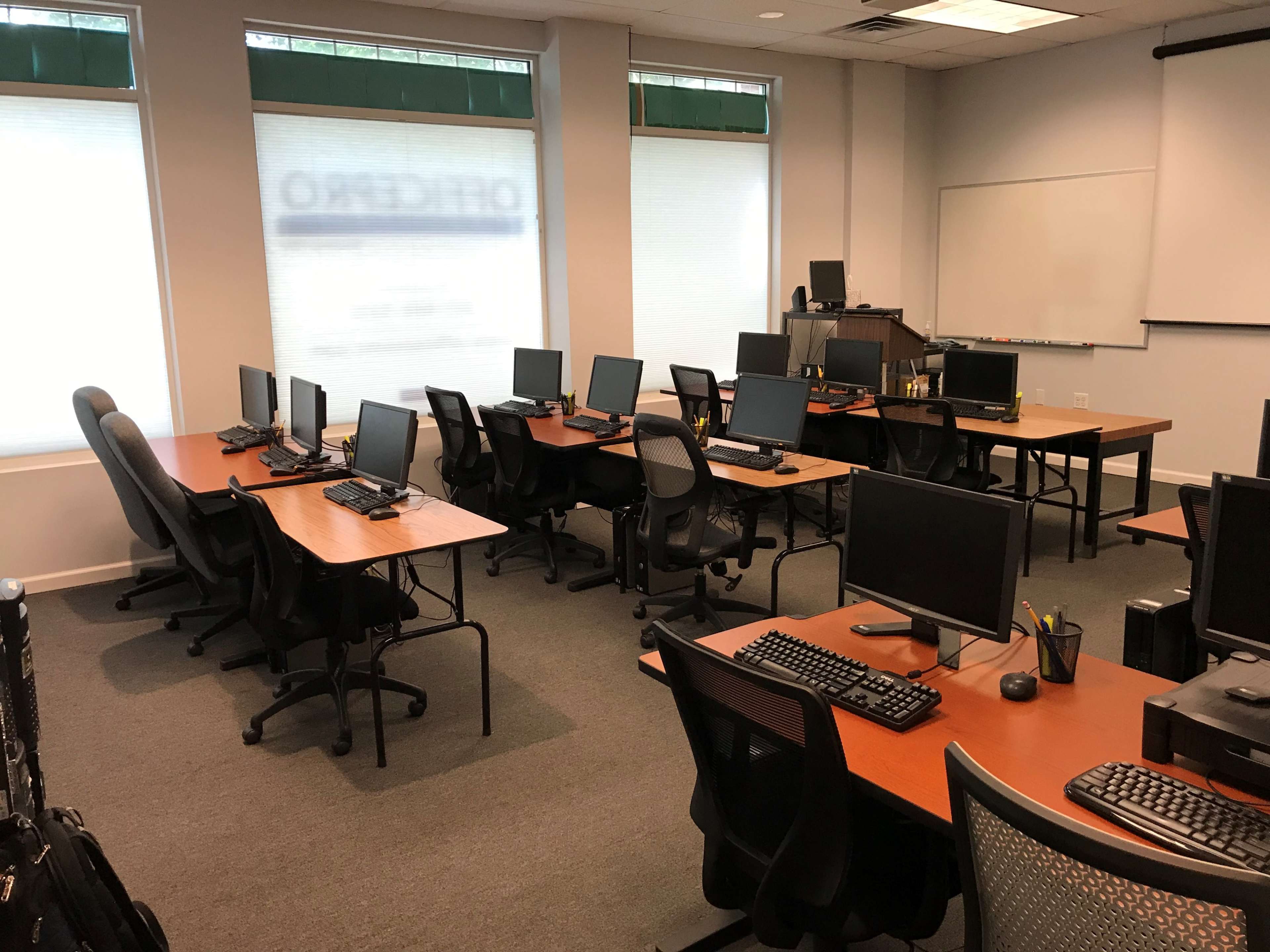 A classroom with several desks, each equipped with computers, arranged in a spacious layout.