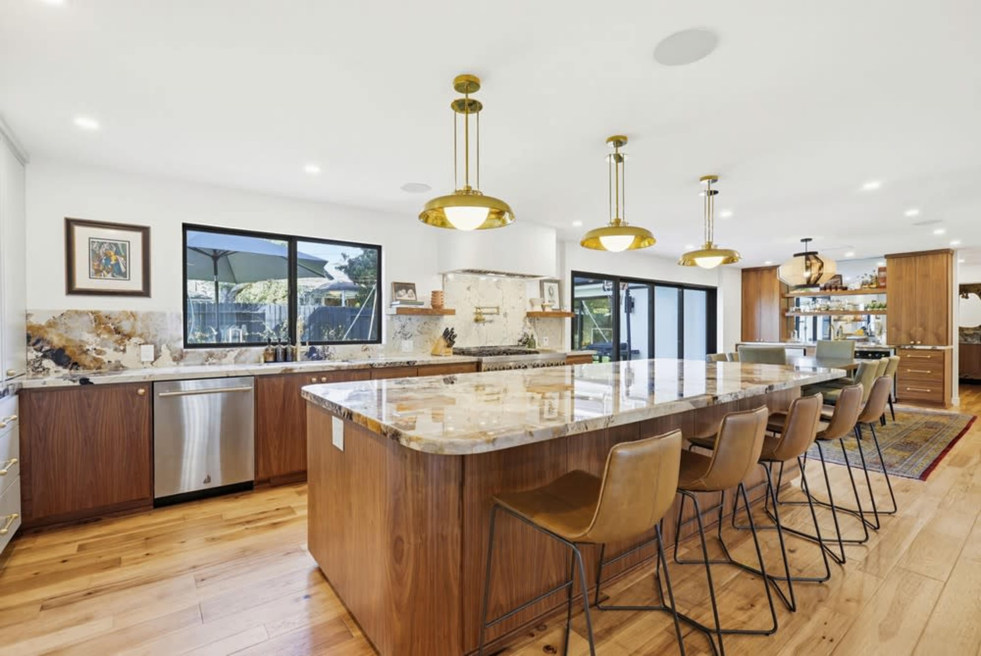 The image shows a modern kitchen featuring a large countertop island with bar stools, gold pendant lights, and ample cabinetry.