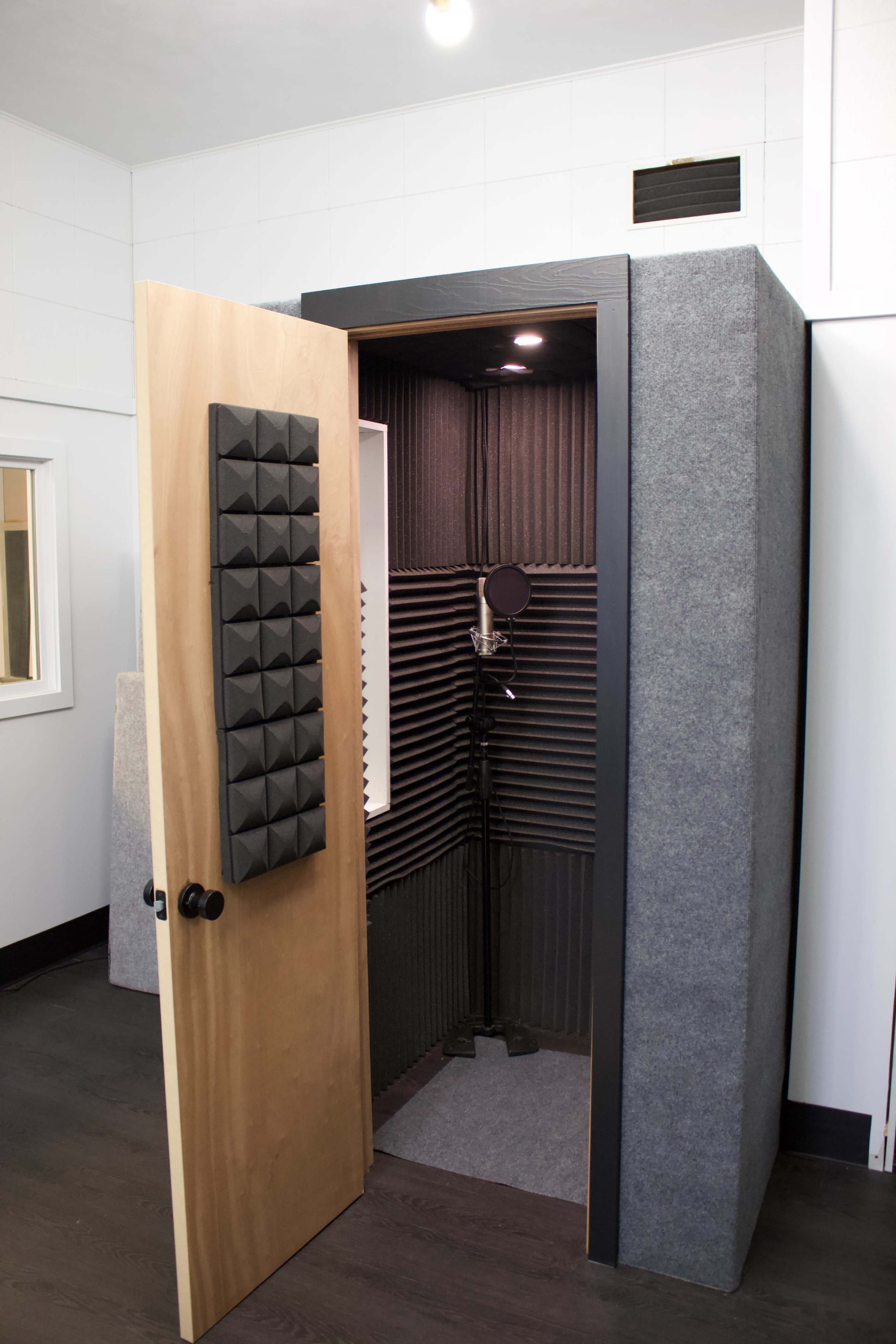 A vocal booth with an open door, featuring soundproofing panels and a microphone inside.