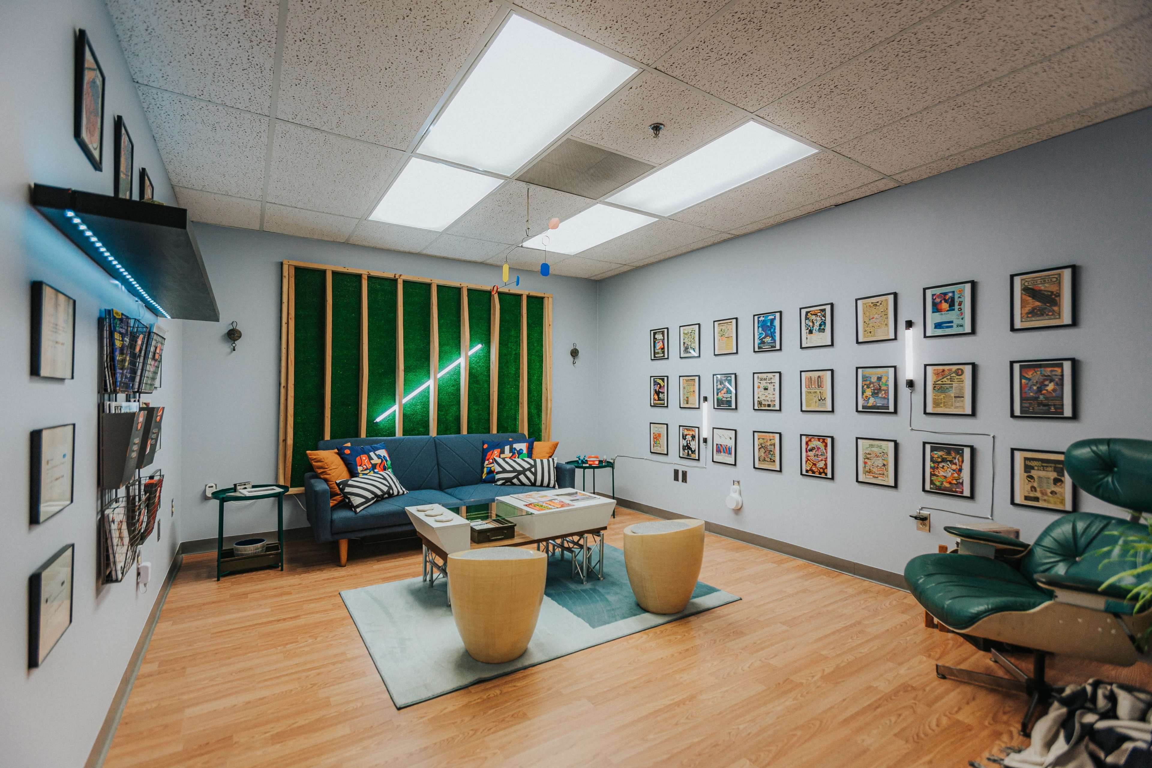 A modern room features a seating area with a couch and coffee table, surrounded by framed artwork on the walls and a green backdrop with ceiling lights.