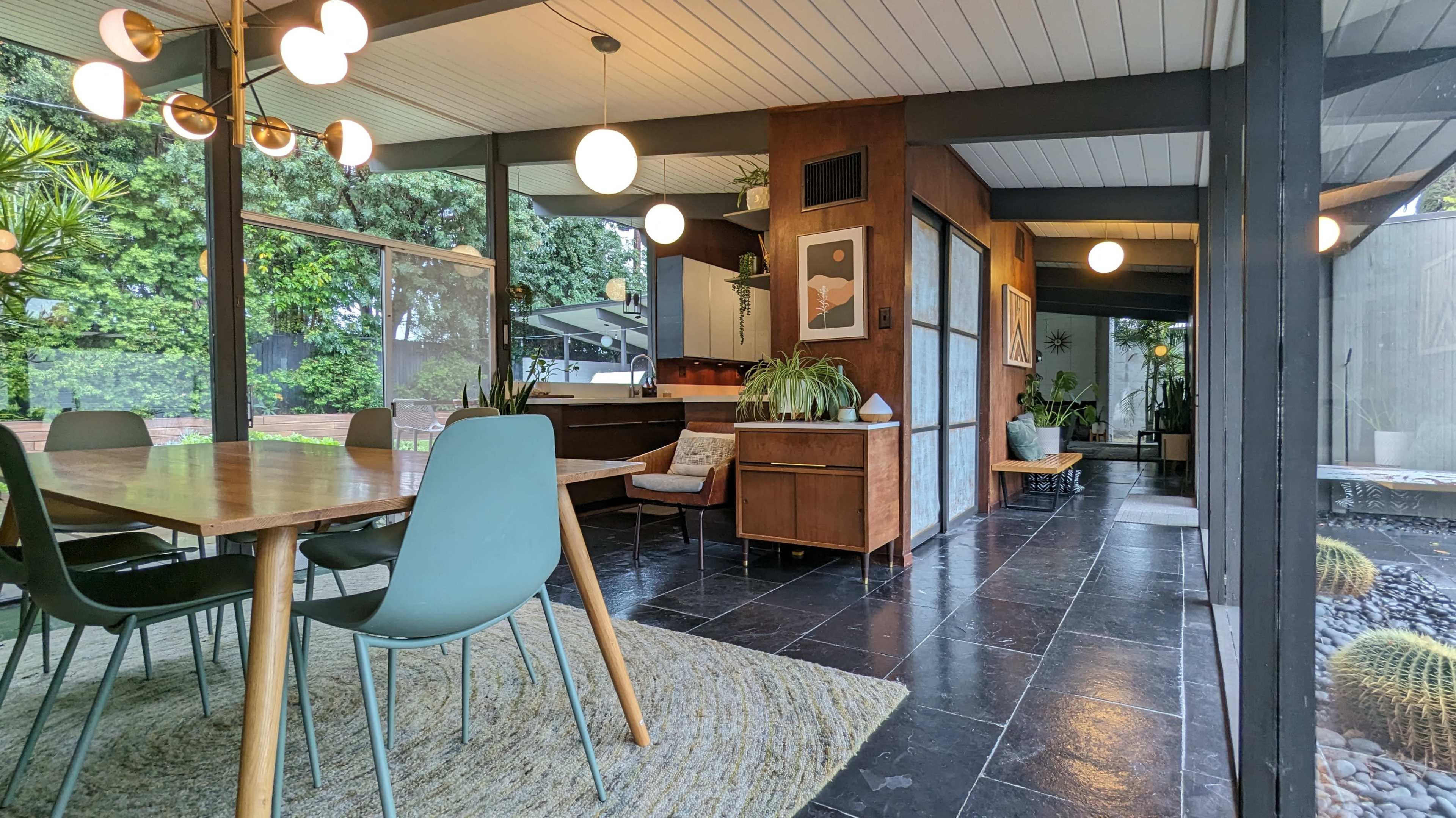 A contemporary dining area with a wooden table, teal chairs, and large windows overlooking a garden.