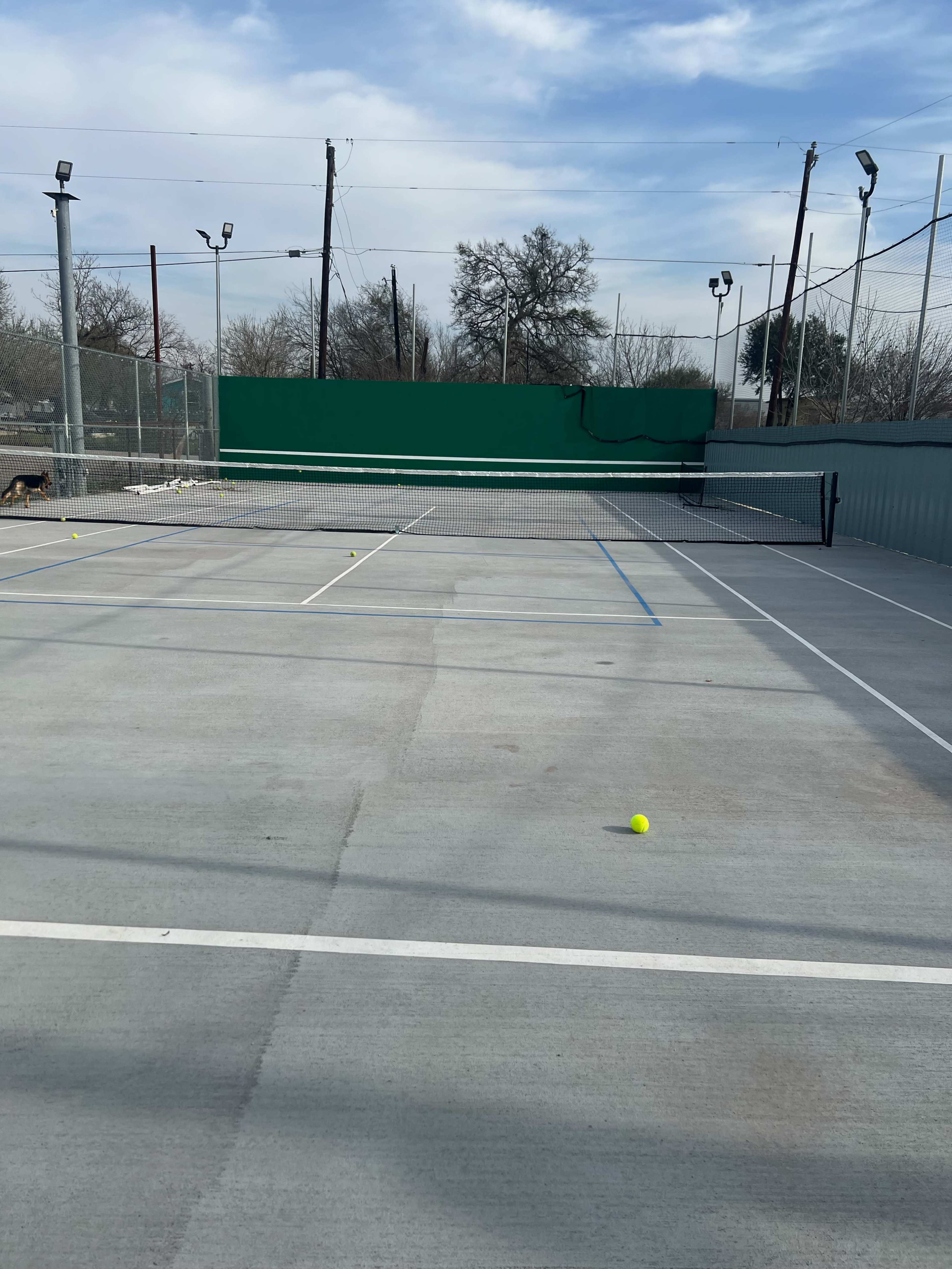 A tennis court with a net in the center and scattered tennis balls on the gray concrete surface.