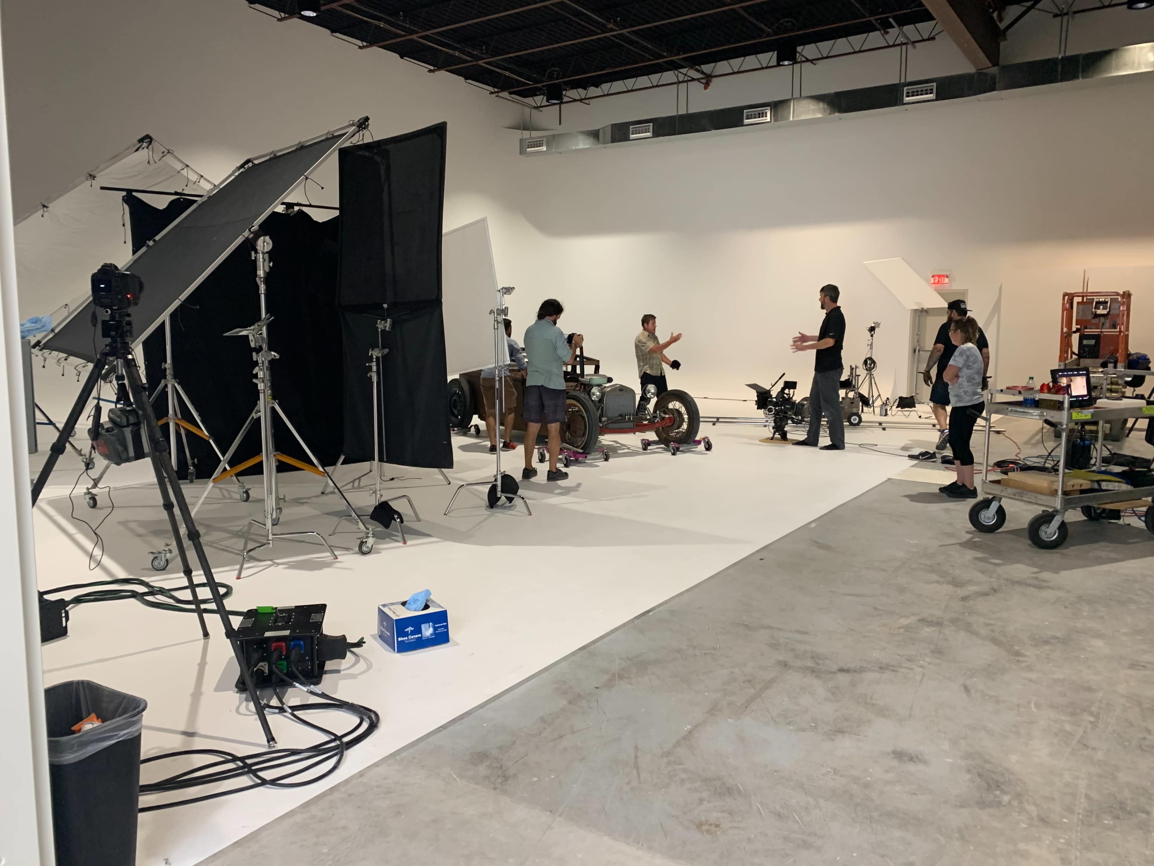 A film or photography studio is set up with various equipment and a team of people working around a central area featuring a motorcycle.