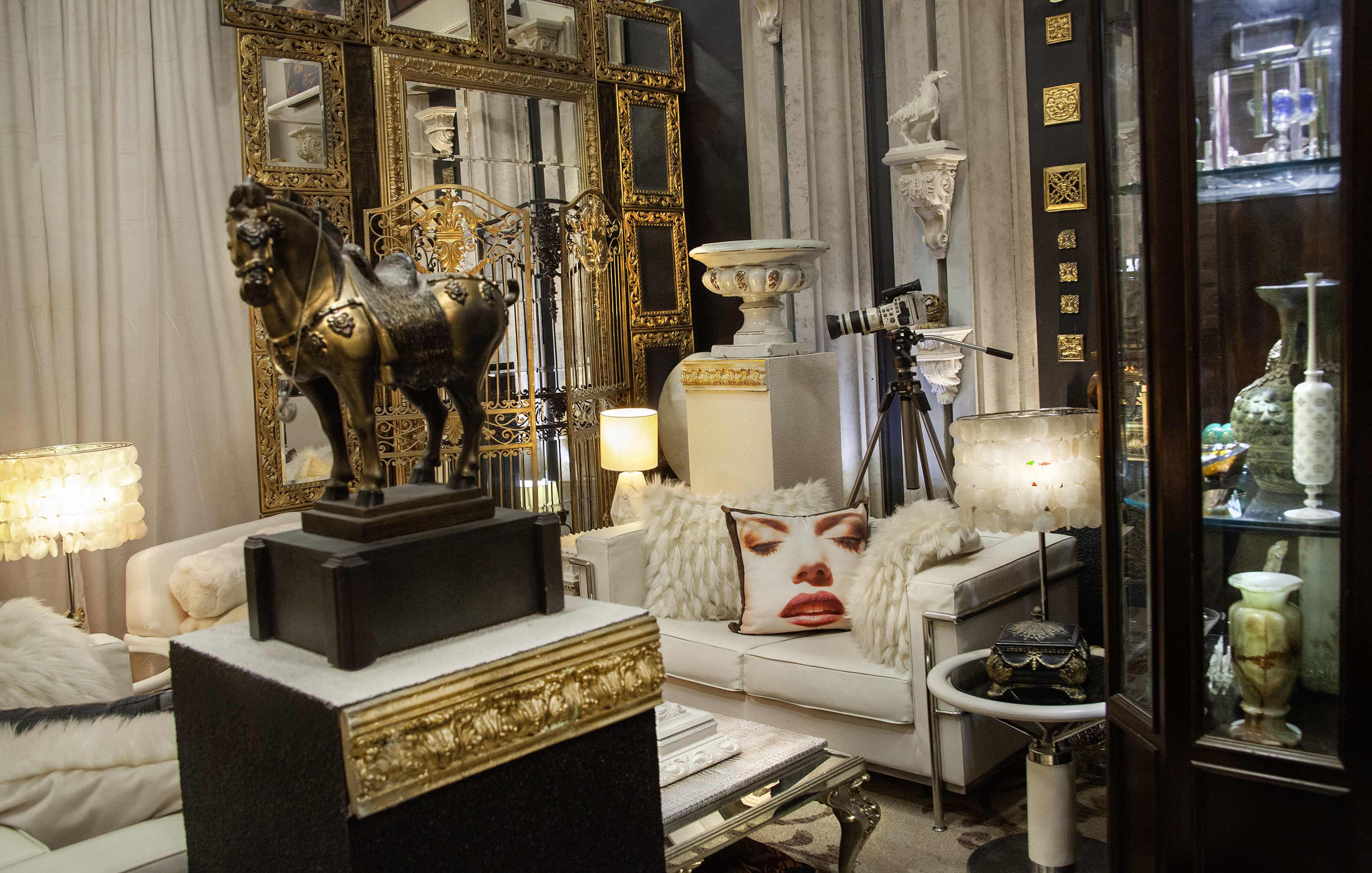 The image displays an elegantly decorated indoor space featuring vintage furniture, ornate mirrors, and various decorative items, including a statue of a horse and unique lighting fixtures.