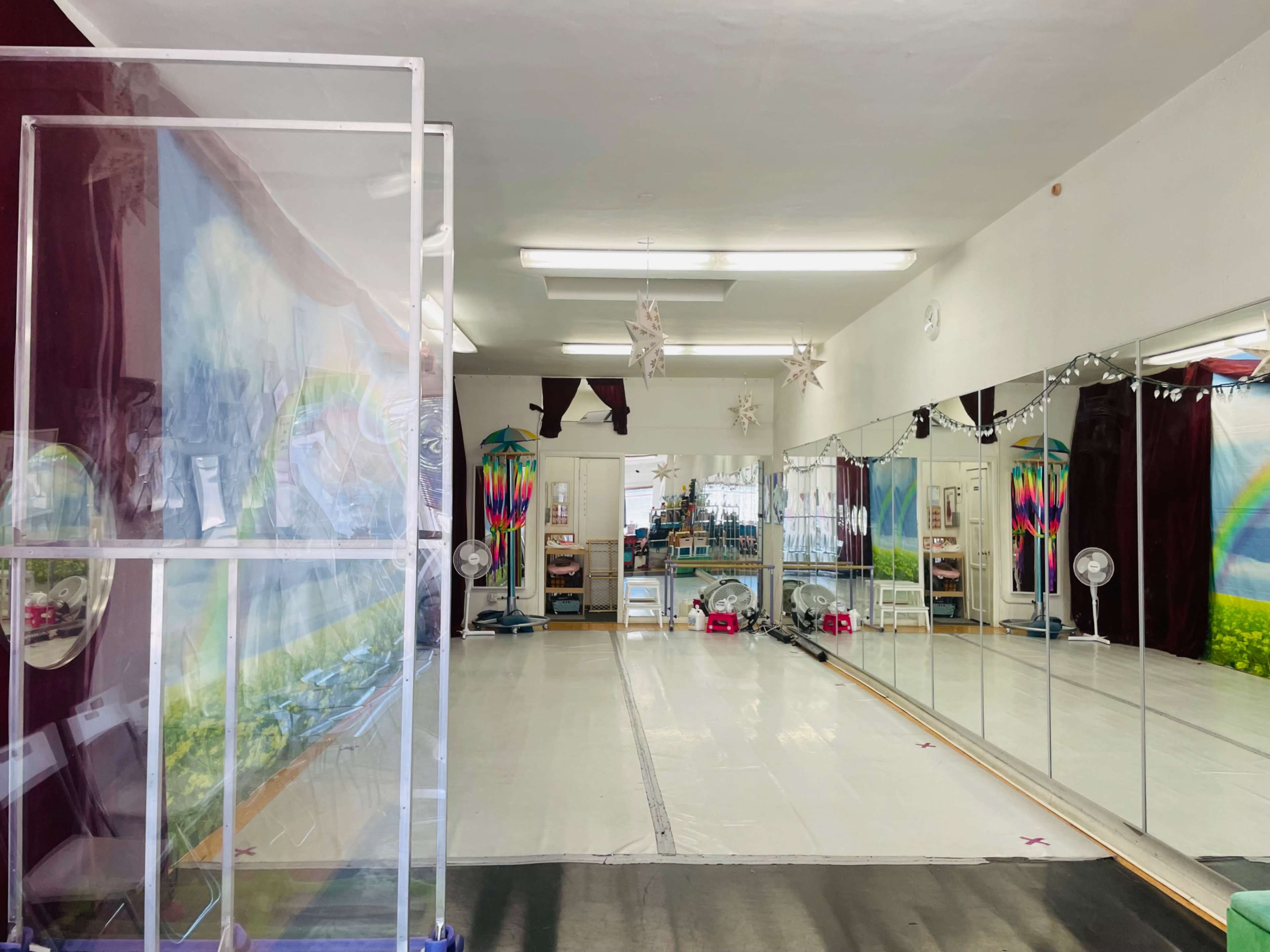 A dance studio featuring mirrored walls, a wooden floor, and decorative elements including a mural and hanging ornaments.