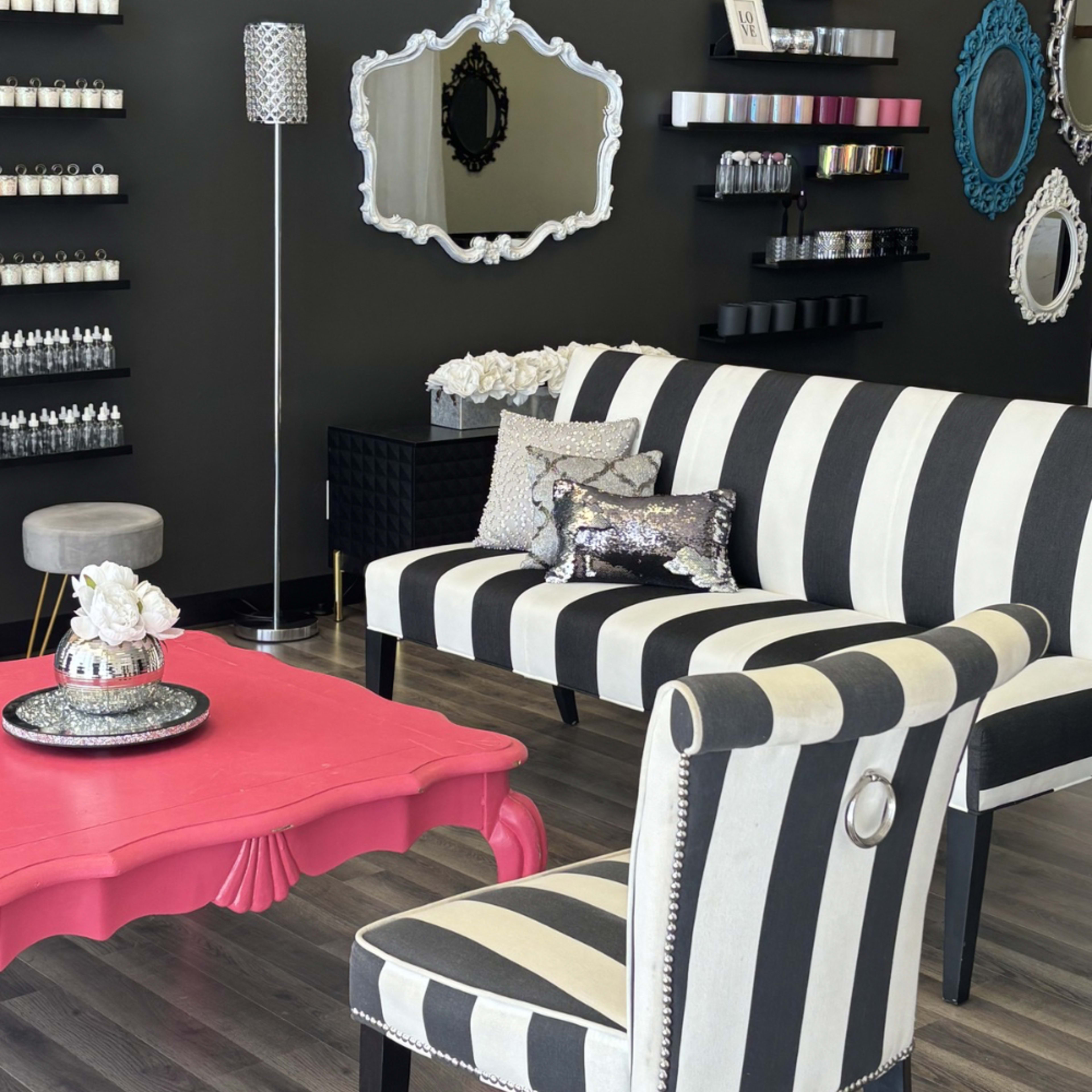 The image shows a modern salon interior featuring black and white striped furniture, a pink coffee table, and decorative items on a dark wall.