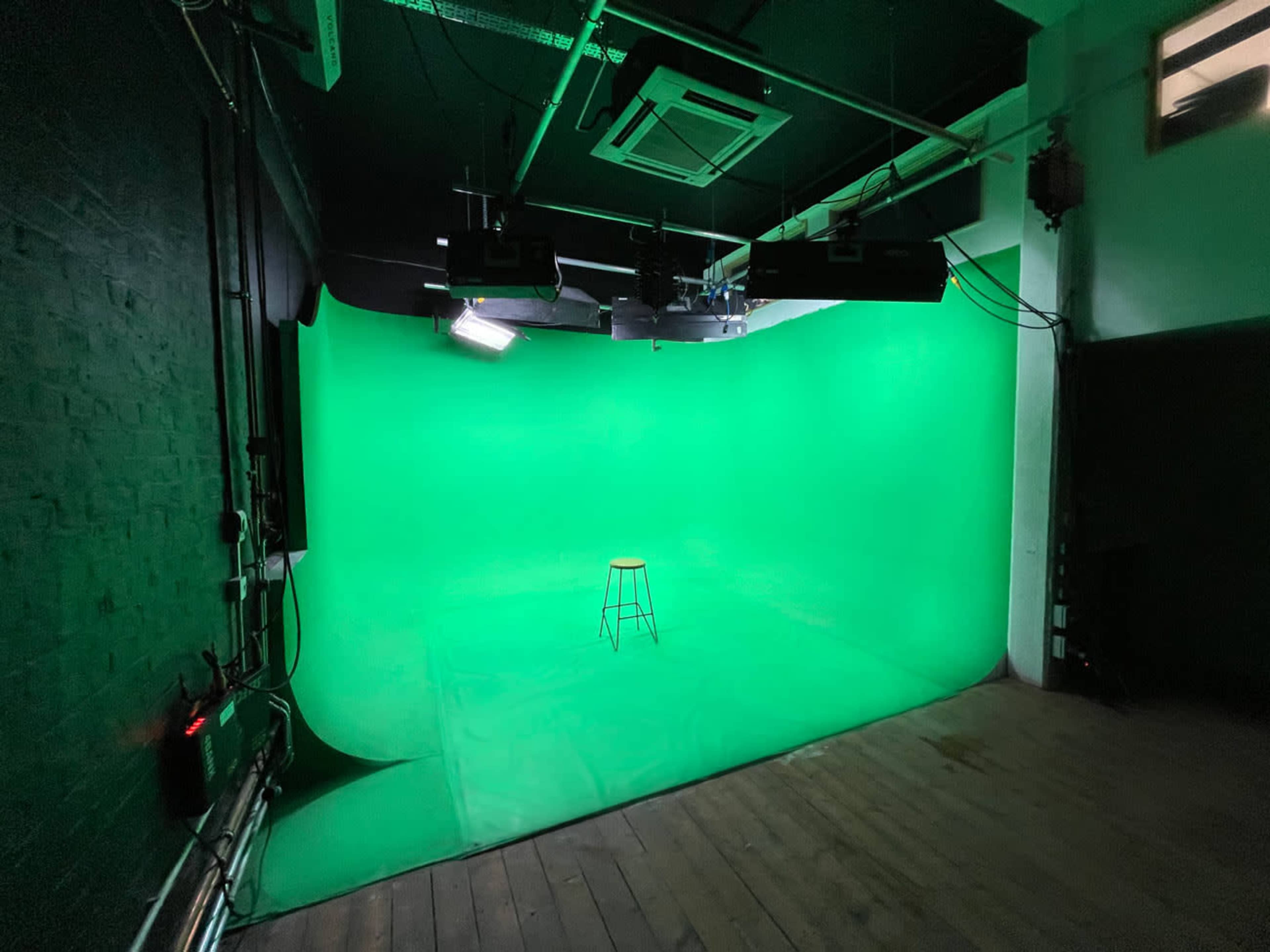 A vacant green screen studio with a single black stool positioned on a smooth floor.