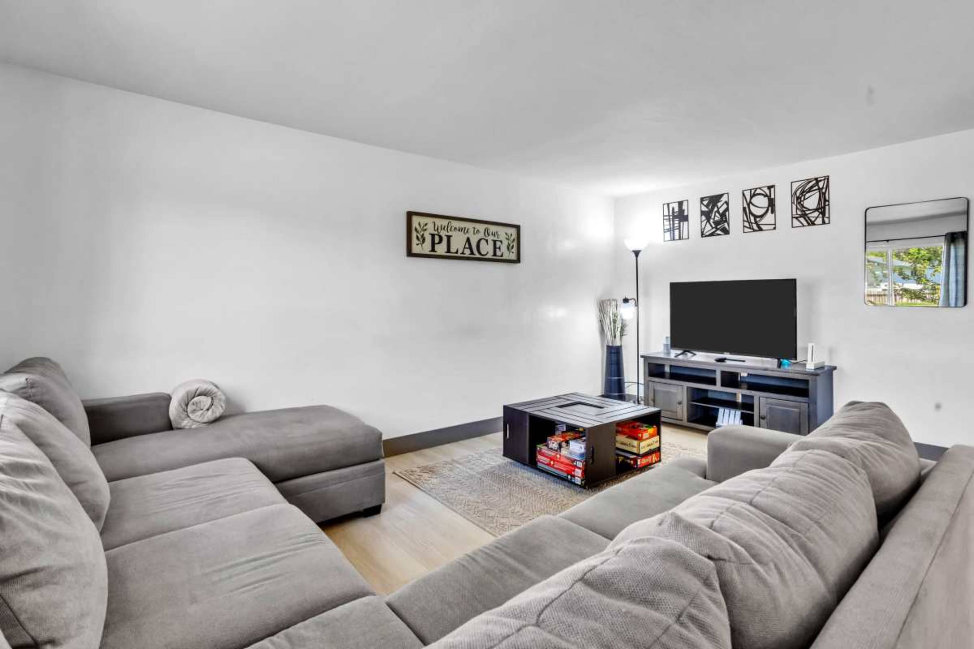 The image shows a modern living room featuring a sectional sofa, a coffee table with books, a television stand, and decorative wall art.