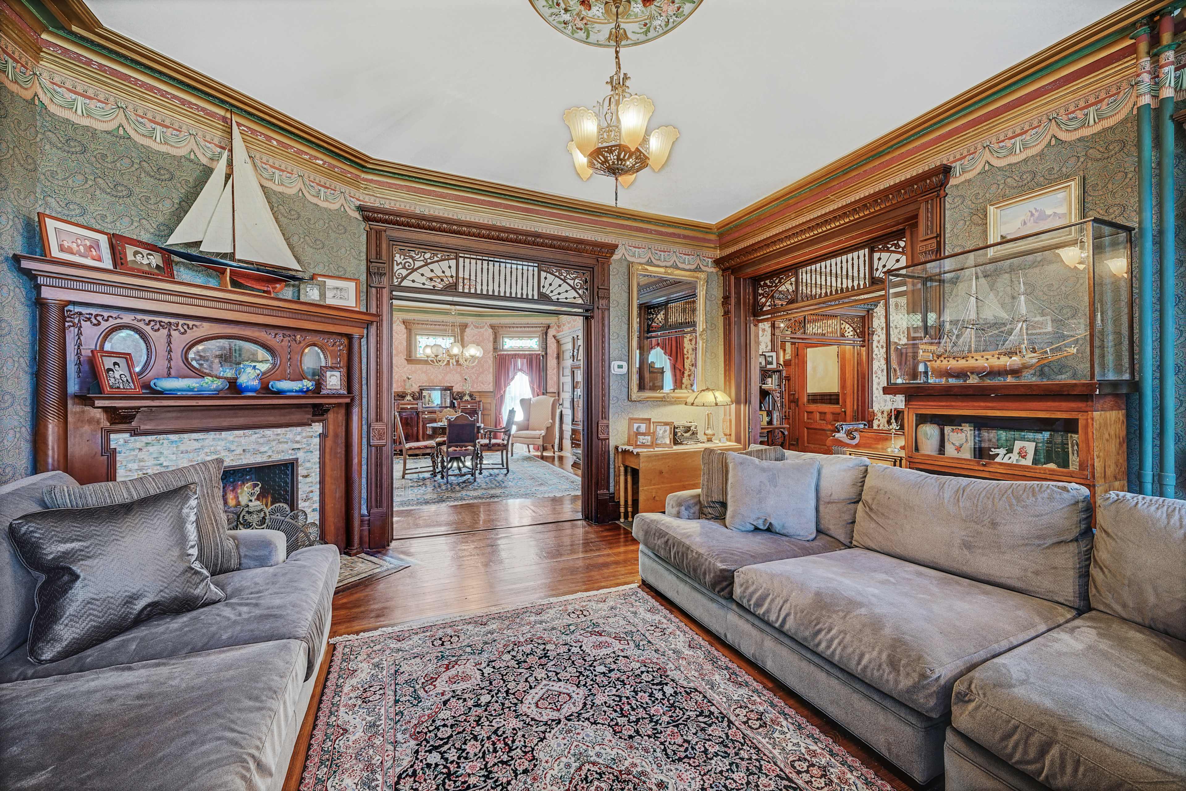 A vintage living room featuring ornate wooden paneling, two plush sofas, and a view of a dining area through an archway.