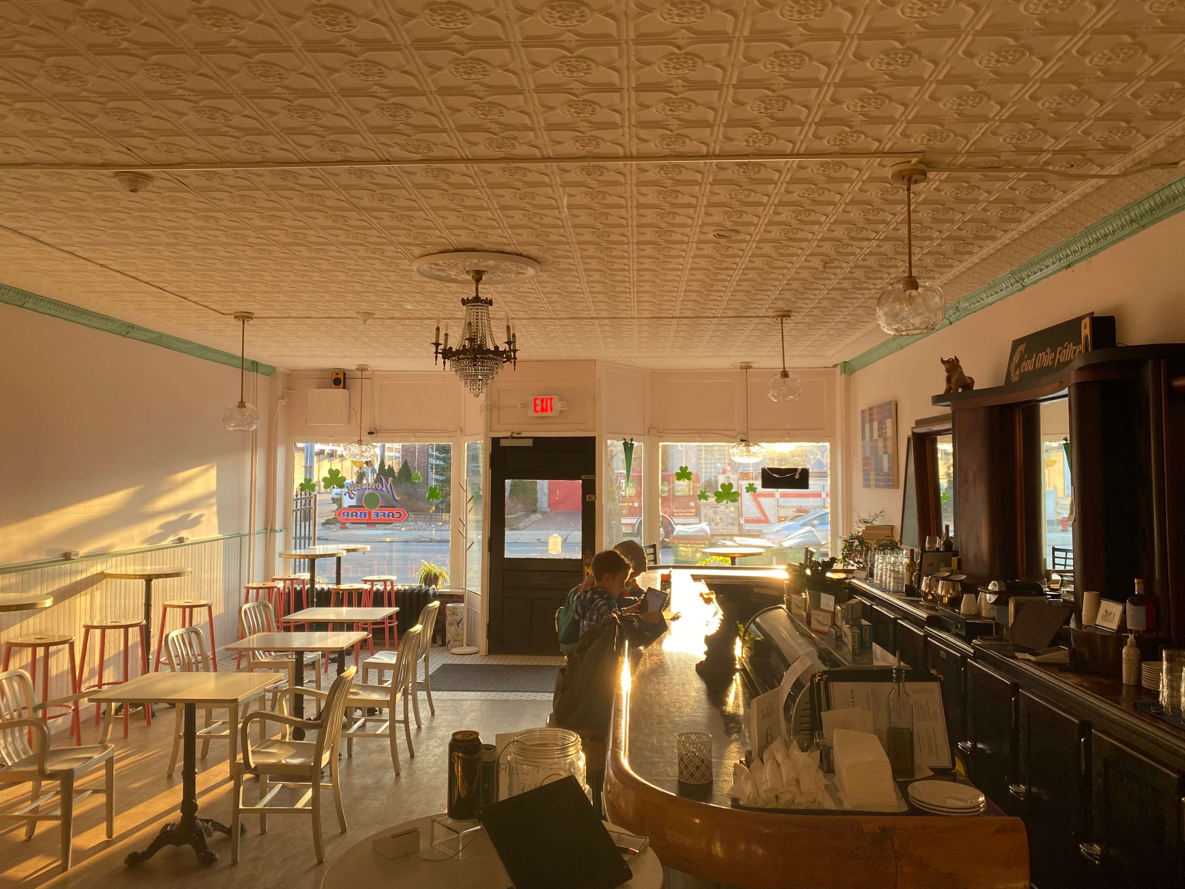 A sunlit café interior features a bar area, tables, and a person standing at the counter.