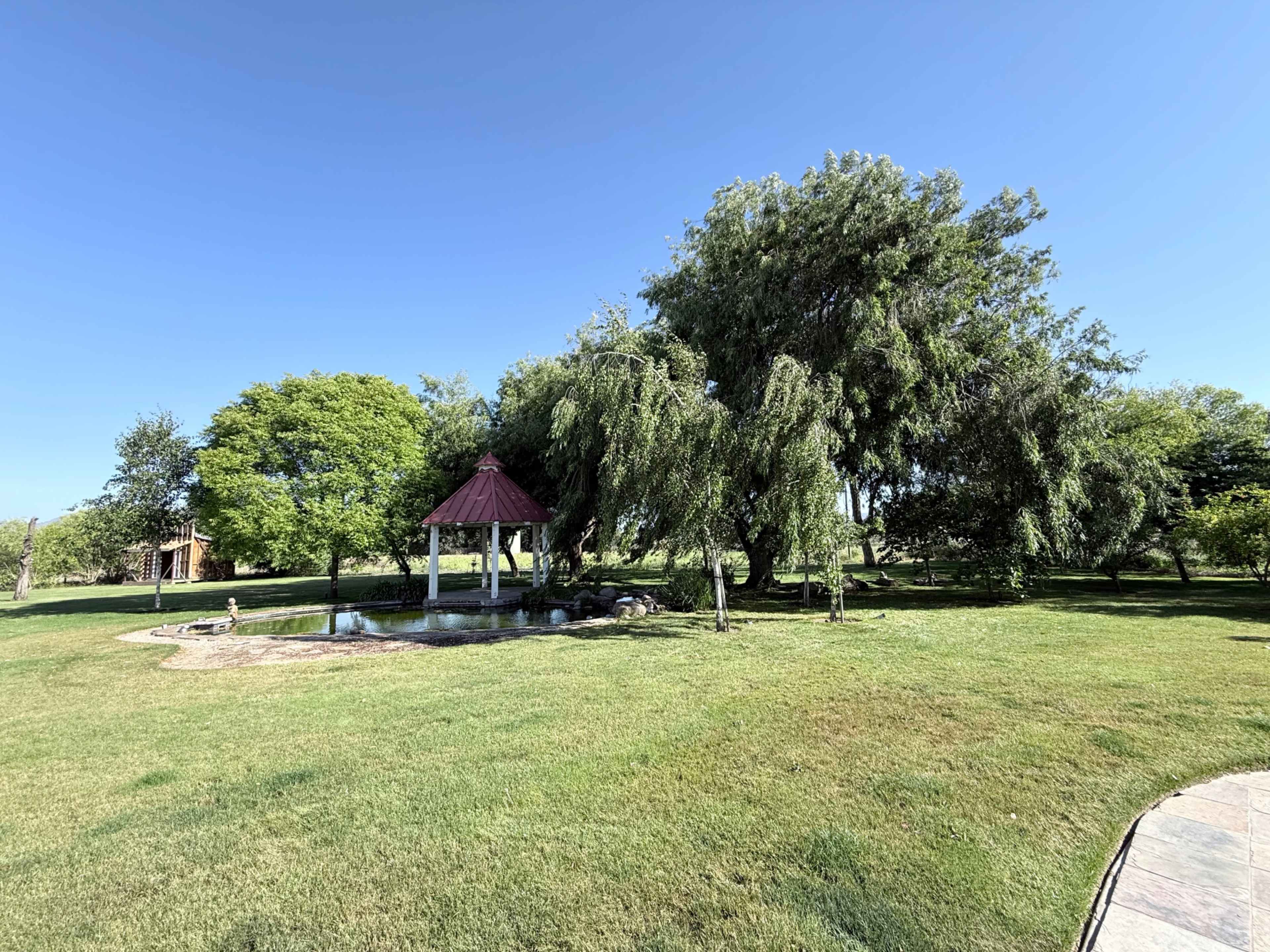 A gazebo with a red roof stands near a small pond surrounded by lush green grass and trees.